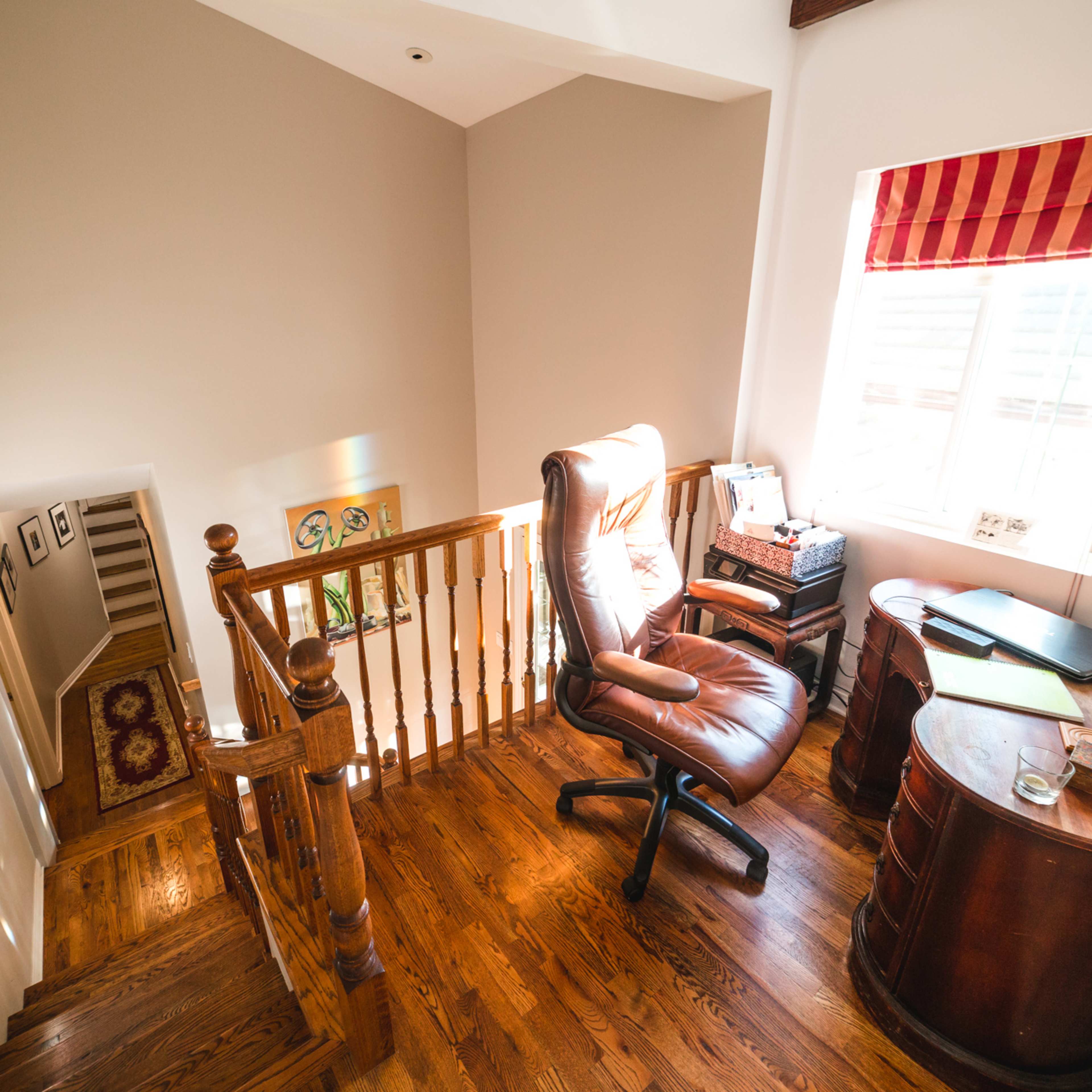 A well-lit stairway leading to a landing with a leather chair, a desk, and framed photographs on the walls.