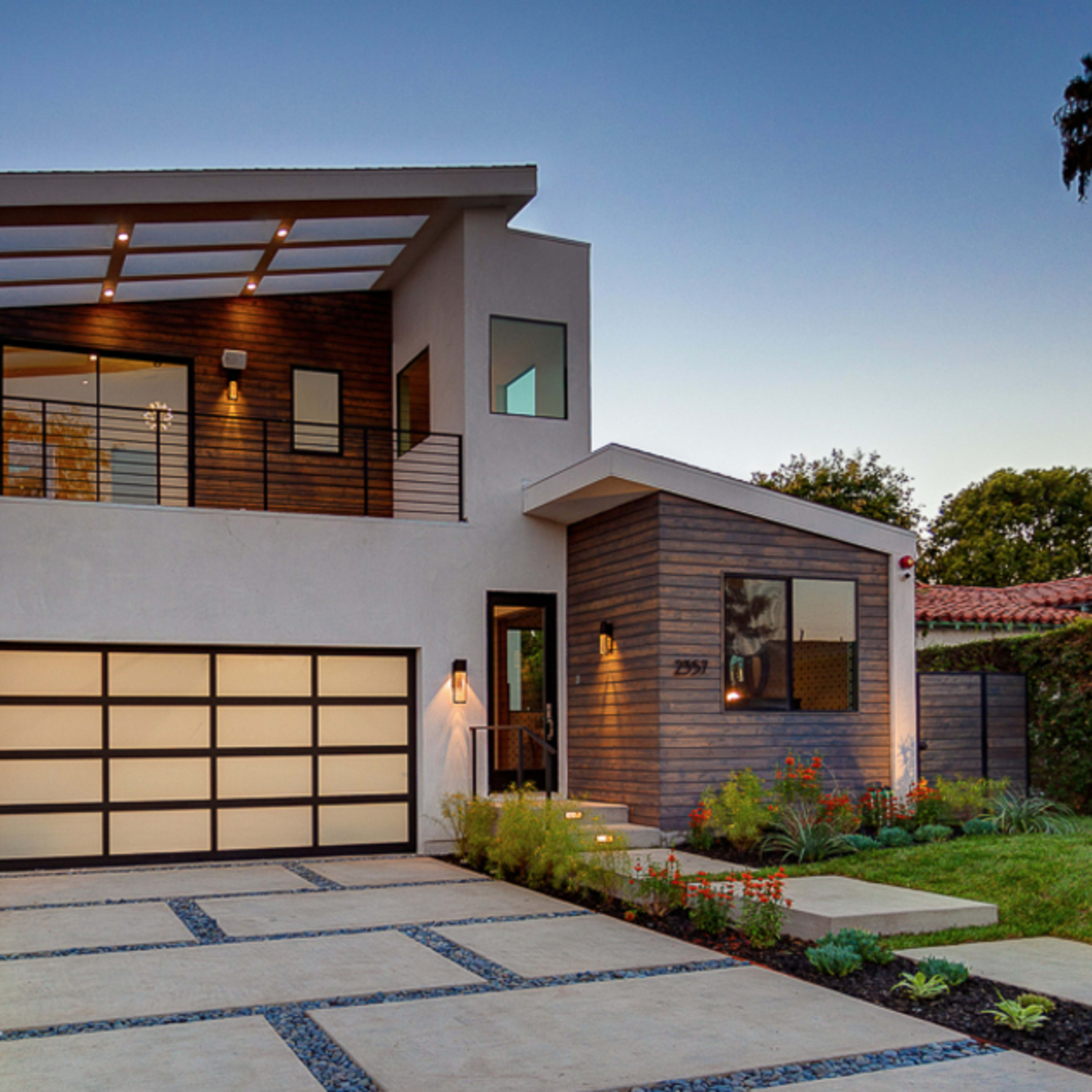 A modern two-story house with a sleek facade, a landscaped front yard, and a driveway leading to a garage.