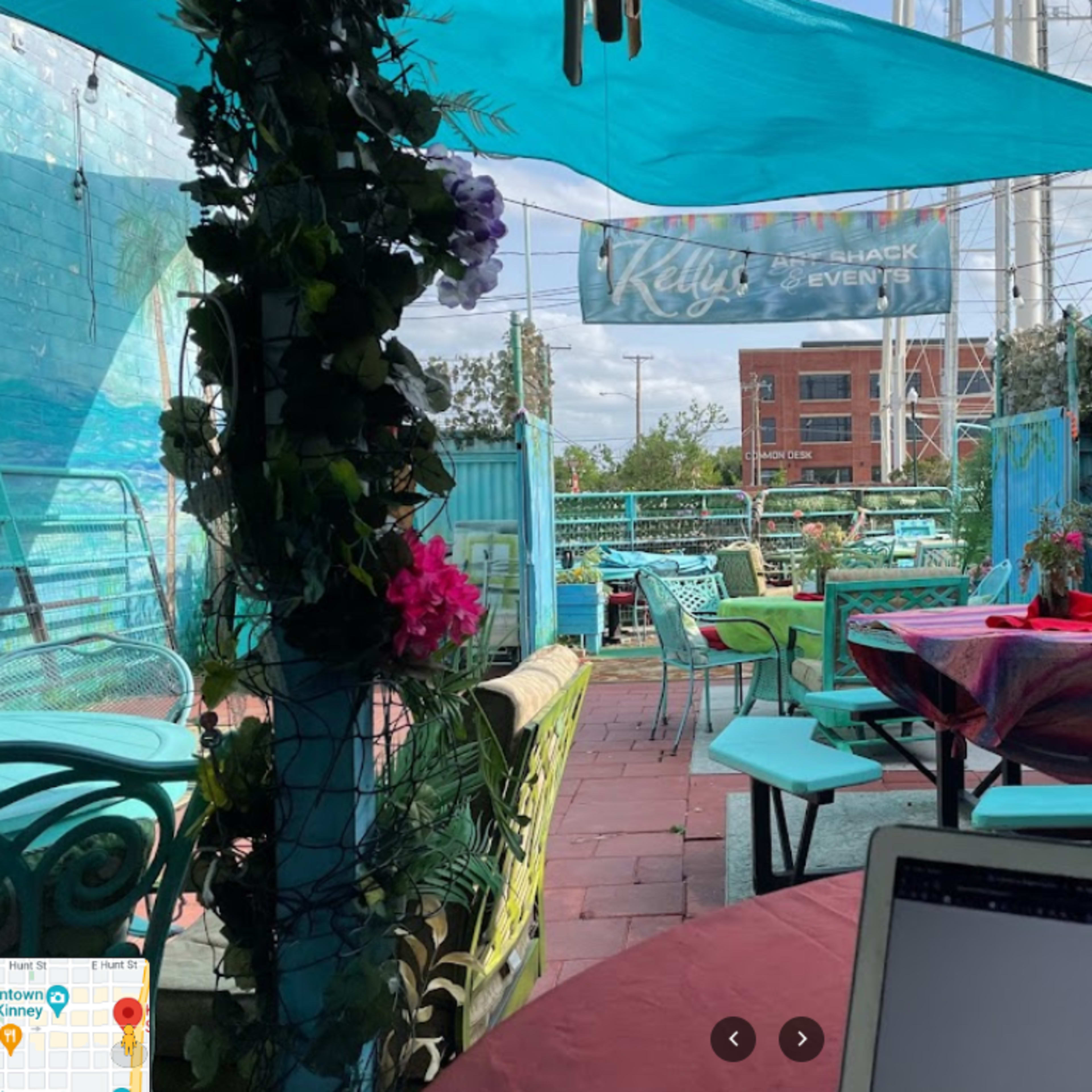 A colorful outdoor patio with turquoise furniture, tables covered with vibrant tablecloths, and decorated with plants and flowers.