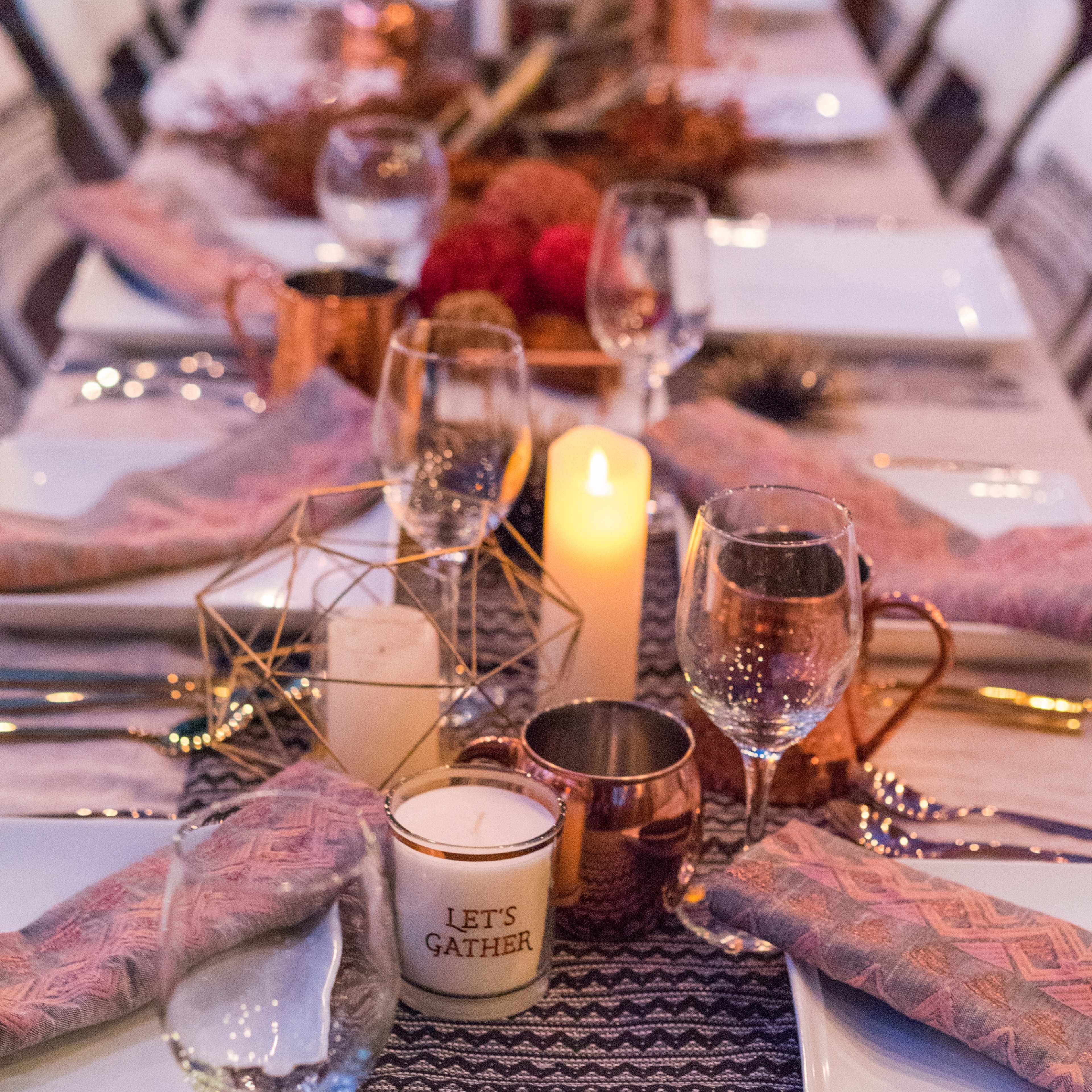 A long dining table is elegantly set with plates, glasses, and decorative elements, including candles and floral arrangements.
