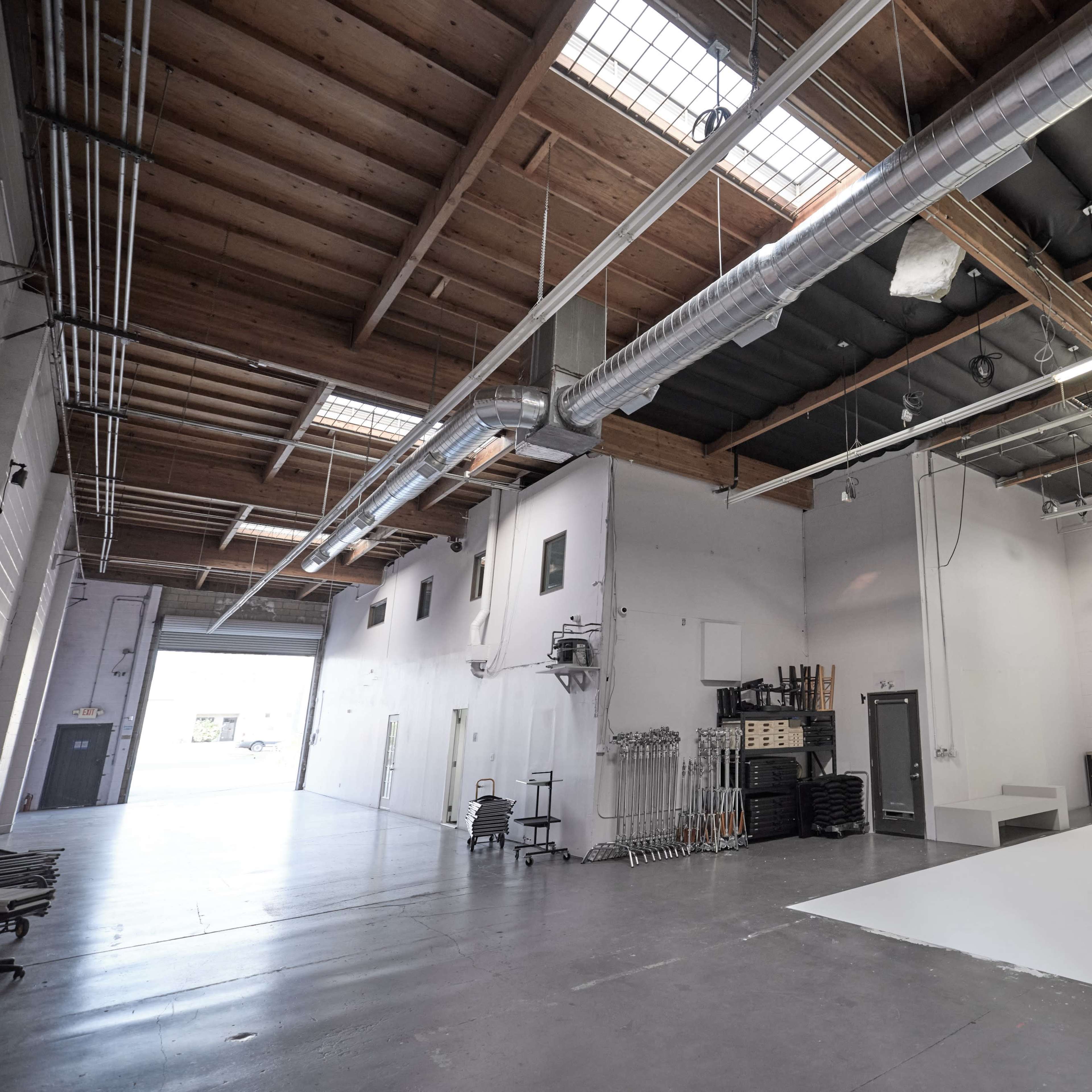 A spacious photography studio with a white backdrop, overhead lighting, and exposed wooden beams.