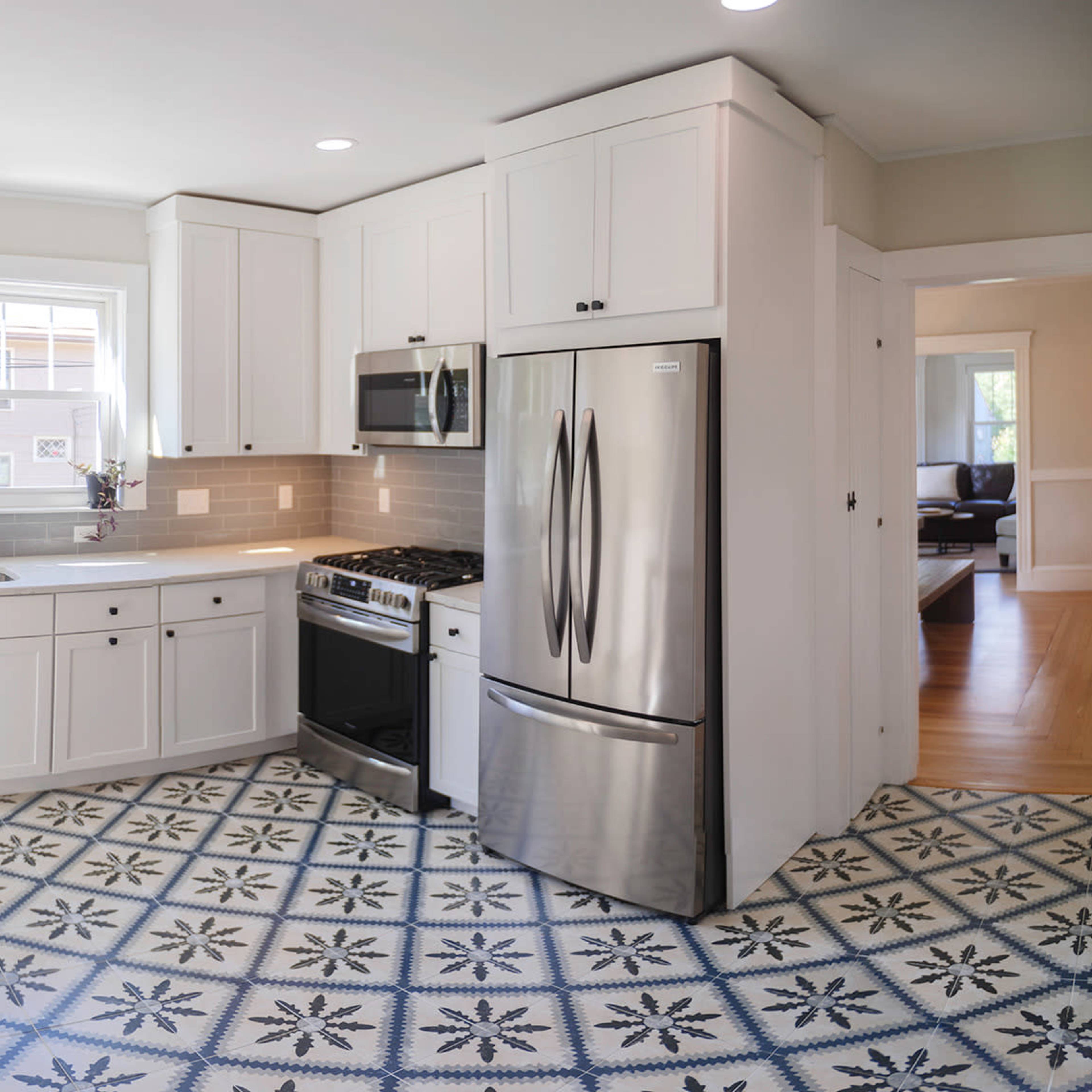 A modern kitchen featuring white cabinetry, stainless steel appliances, and a patterned tile floor.