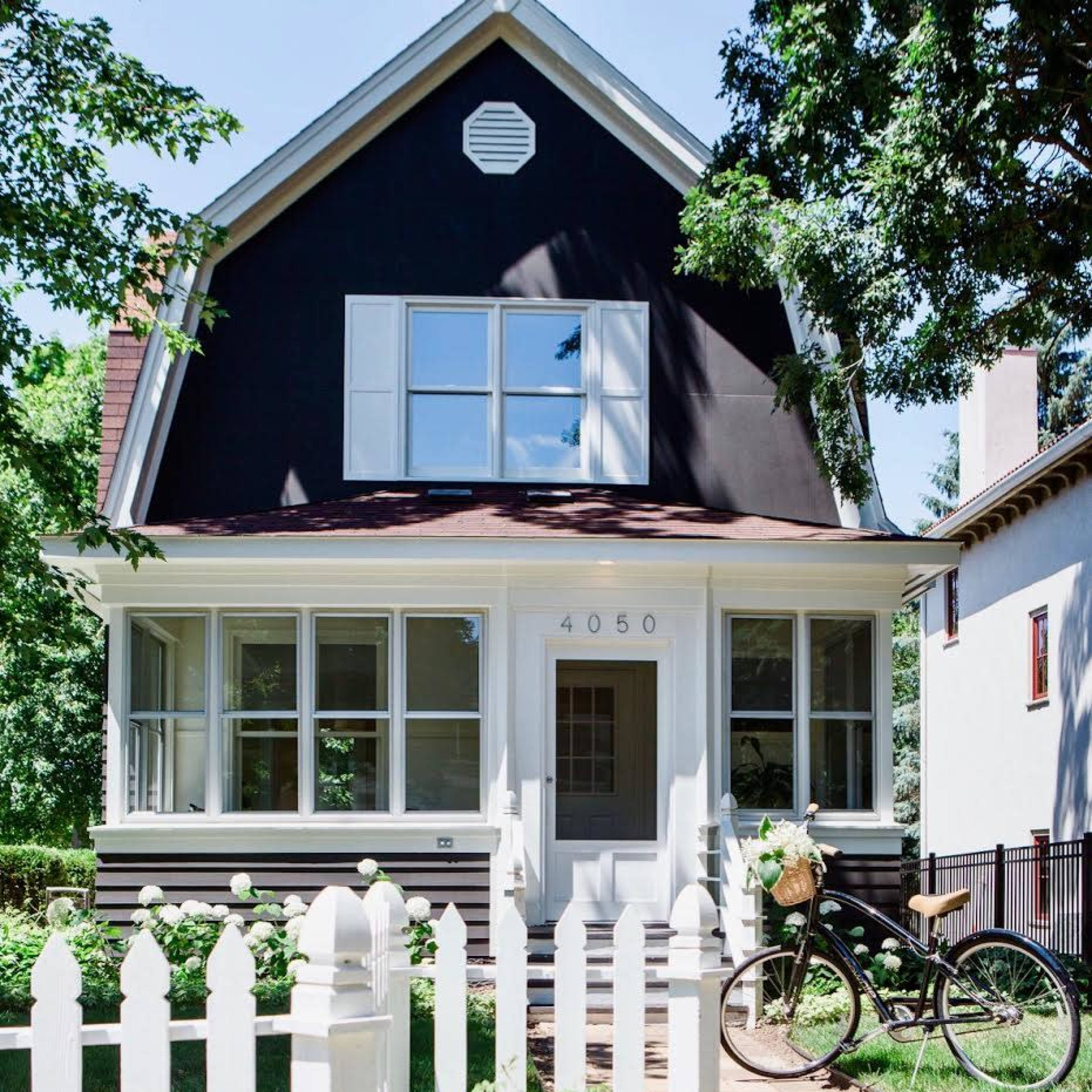 A black-painted house with white trim features a picket fence and a bicycle parked alongside a stone pathway.