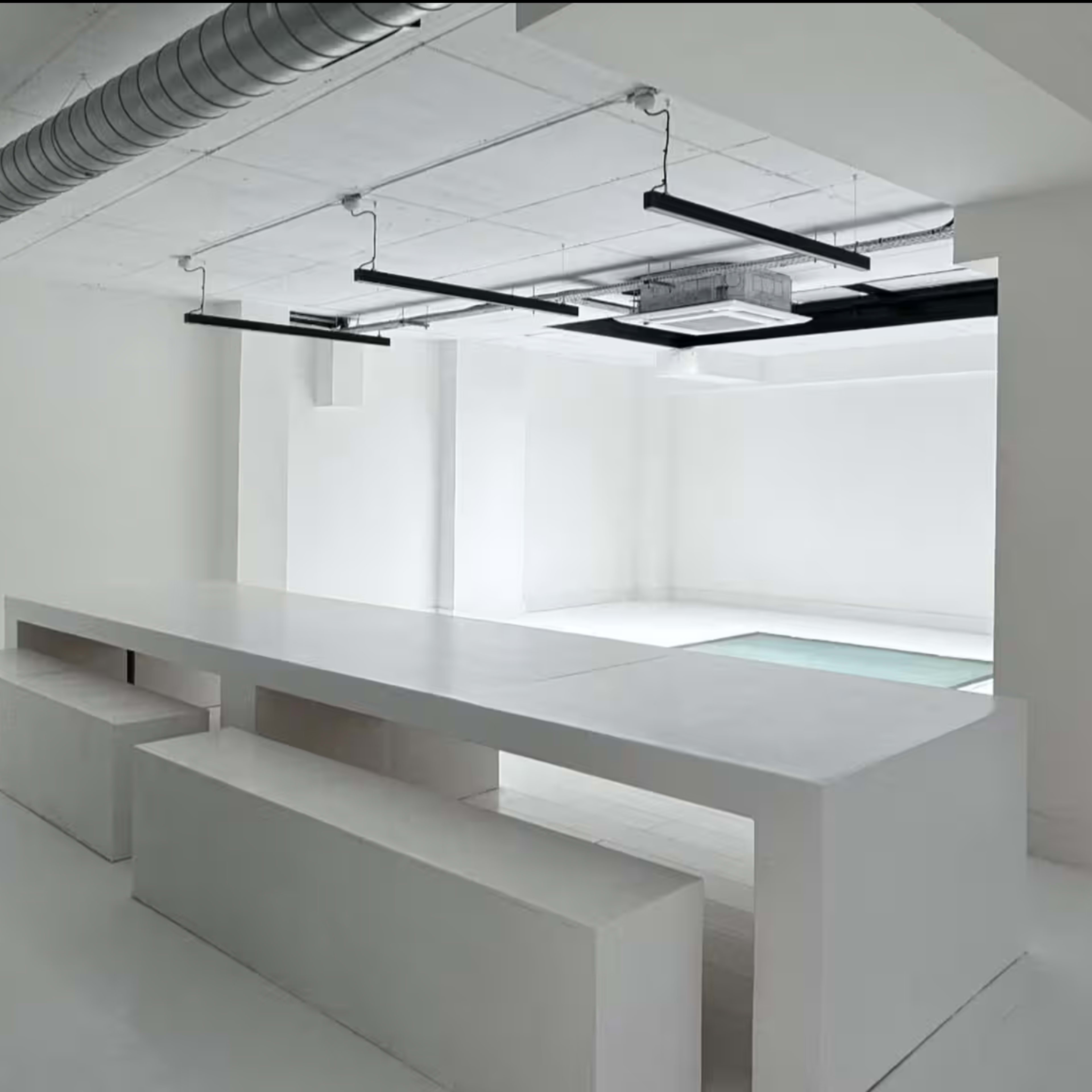 A minimalistic white interior space featuring a long rectangular table and two bench seats.