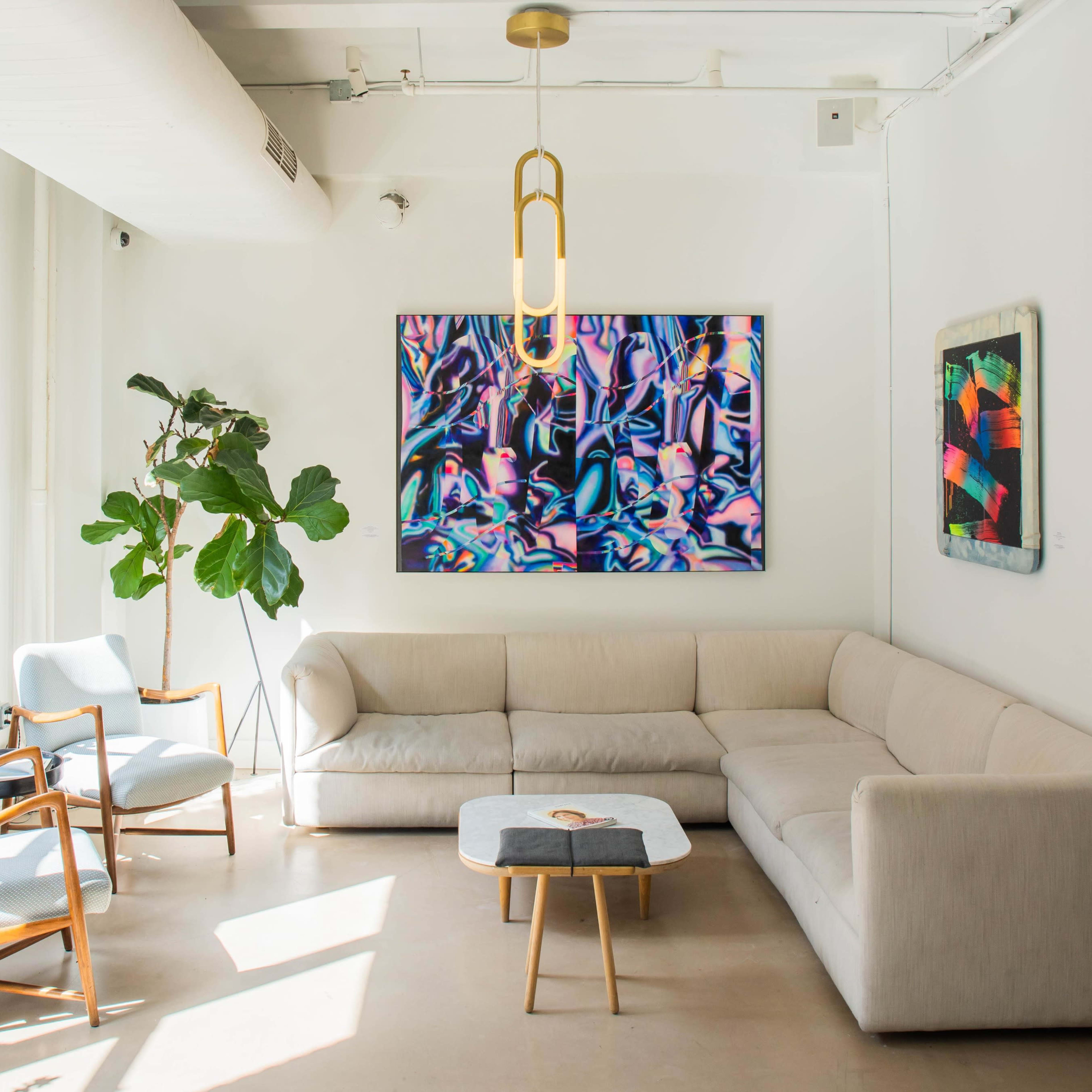 A bright and airy living room features a large sectional sofa, two chairs, a coffee table, and vibrant abstract art on the walls.