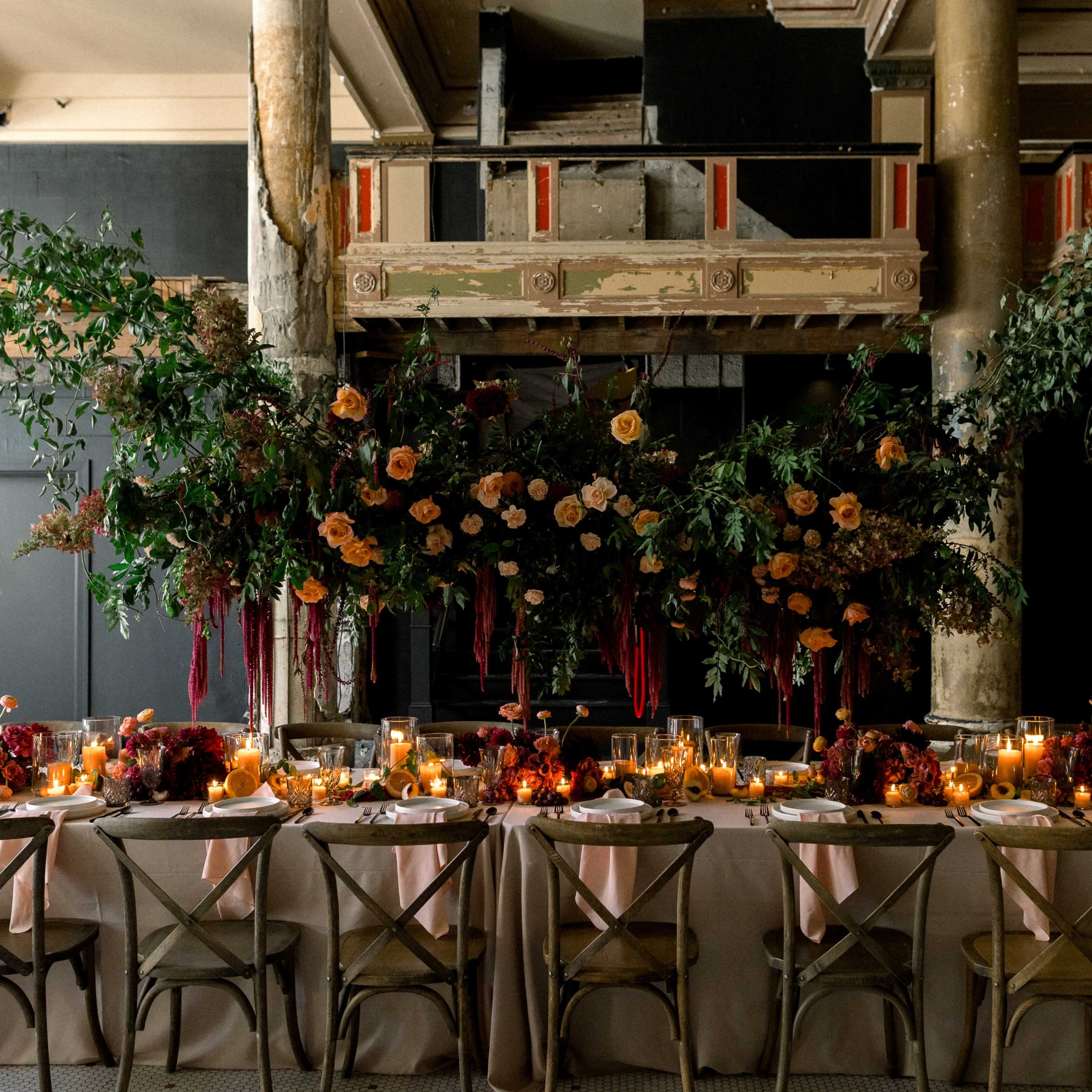 A long table is elegantly set with flowers, candles, and greenery in a spacious, partially renovated venue.