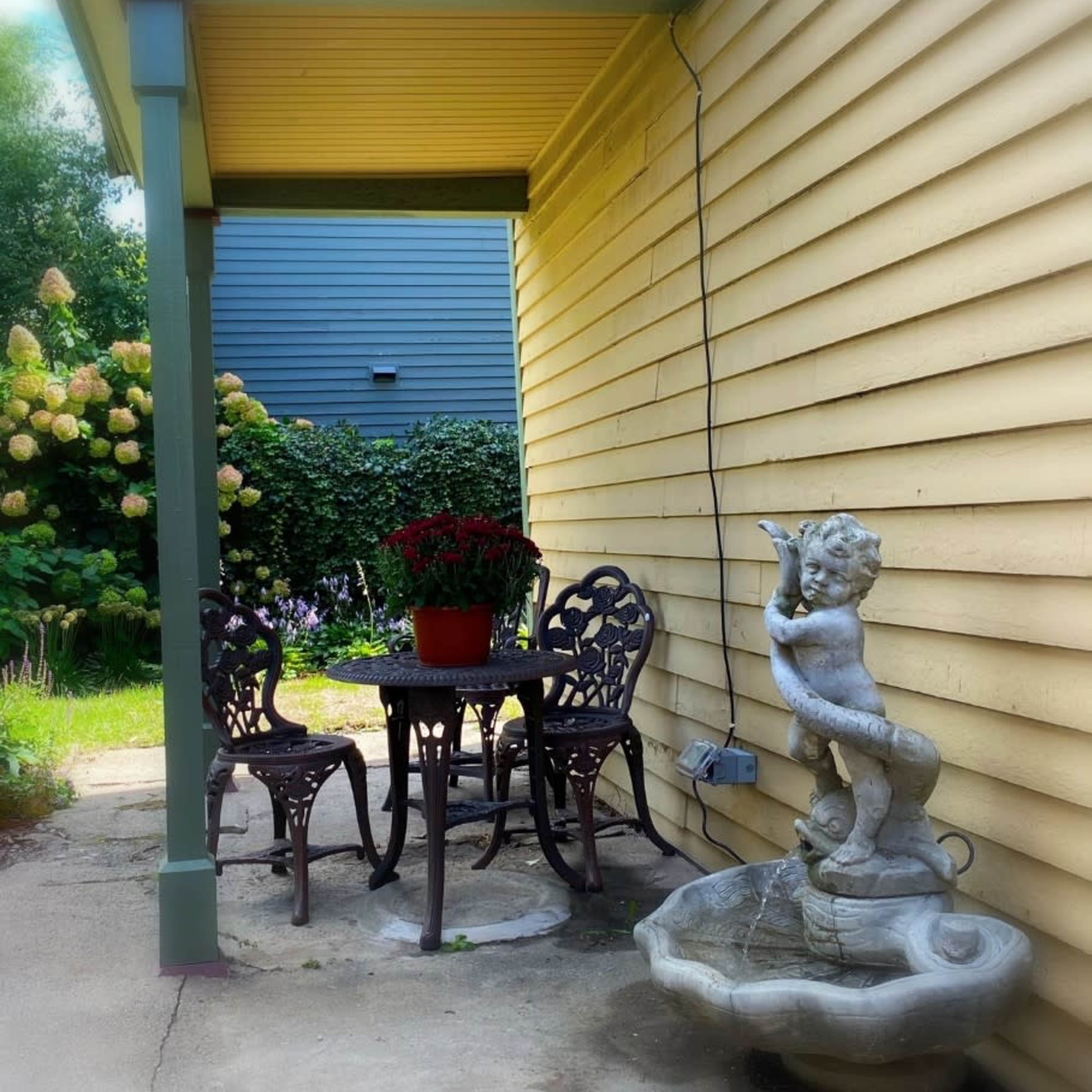 A small outdoor patio area features a table and two chairs beside a decorative fountain with a cherub.