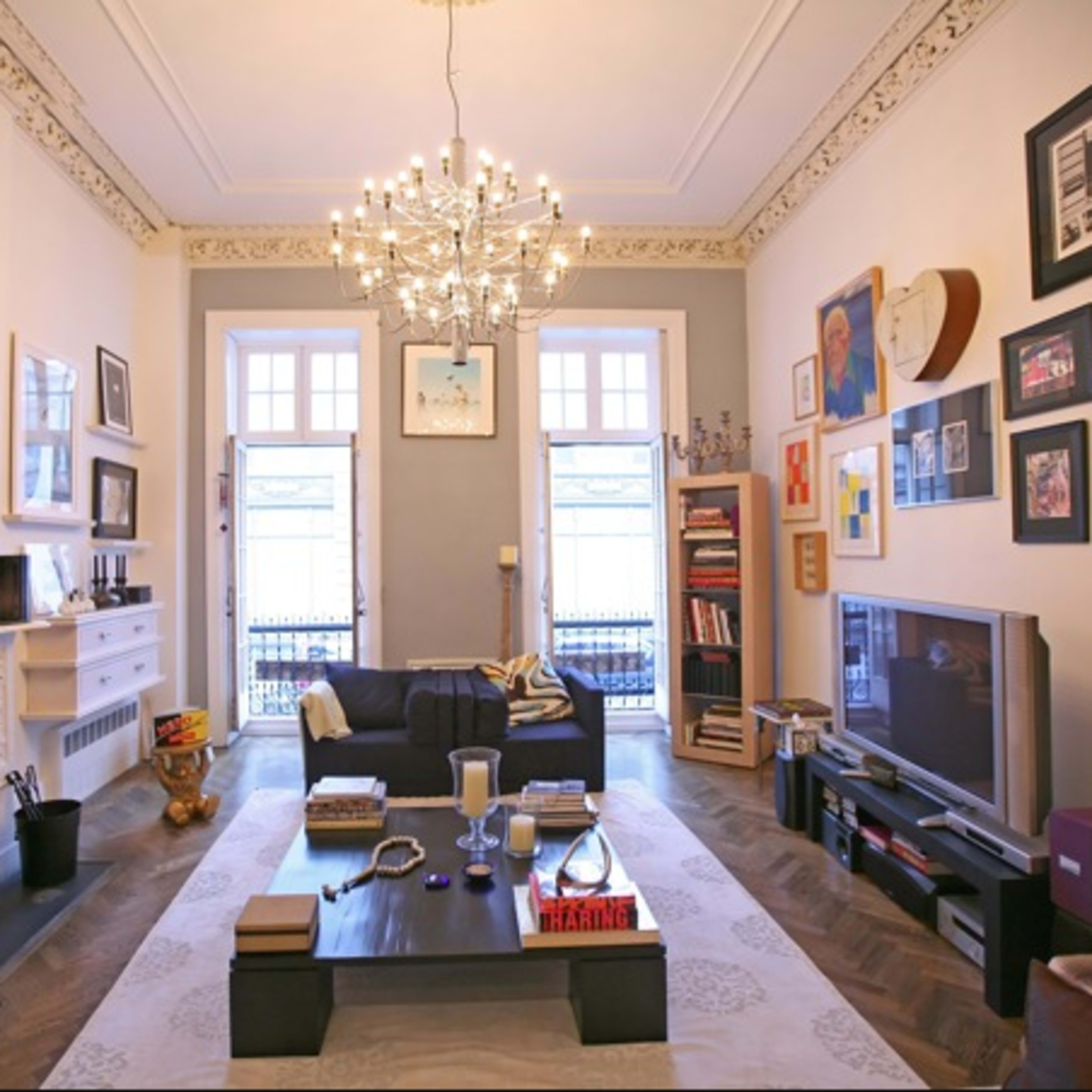 The living room features a chandelier, a dark sofa, a low coffee table, and an array of framed pictures on the walls.