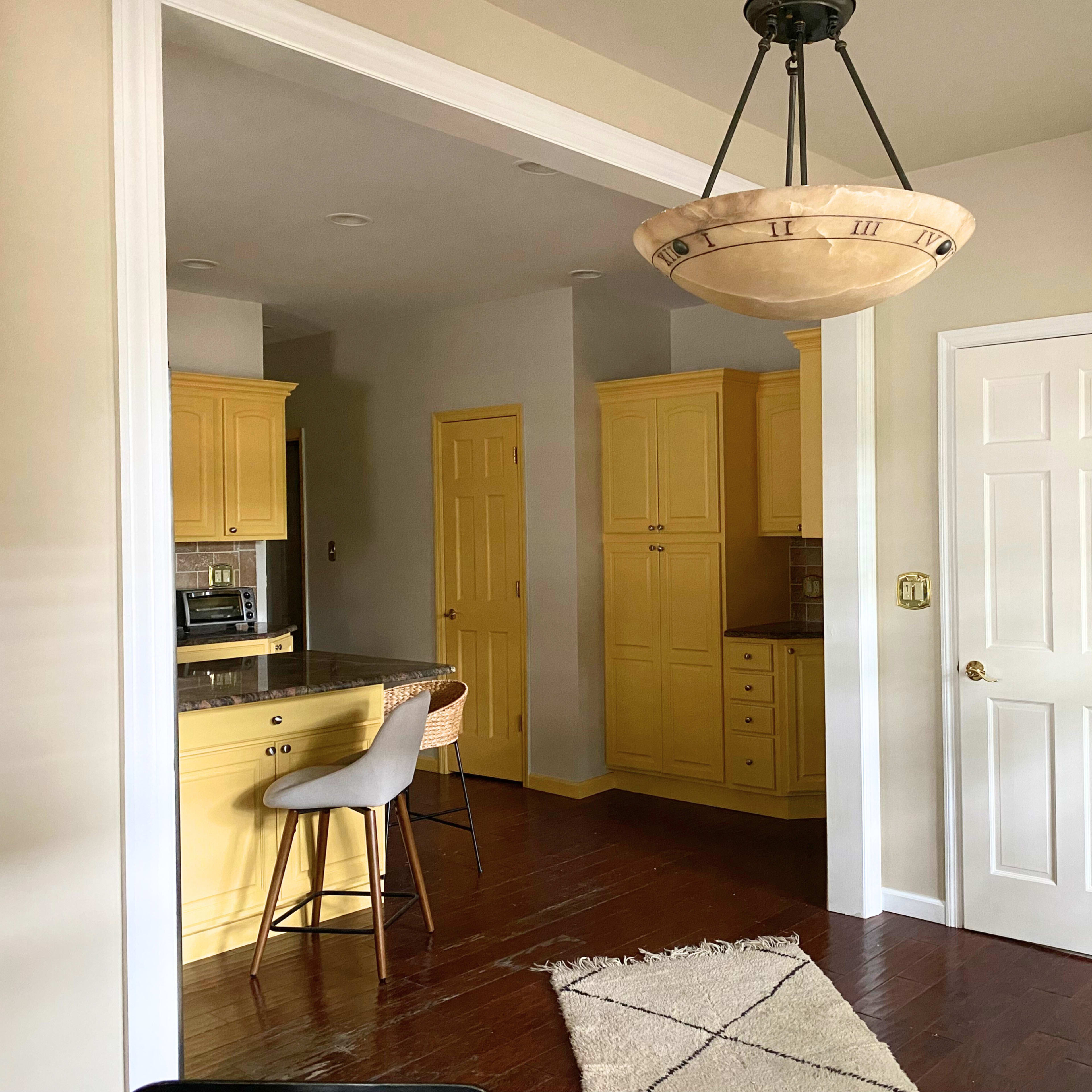 A kitchen area with yellow cabinets, a bar stool at a counter, and a door leading to another room.