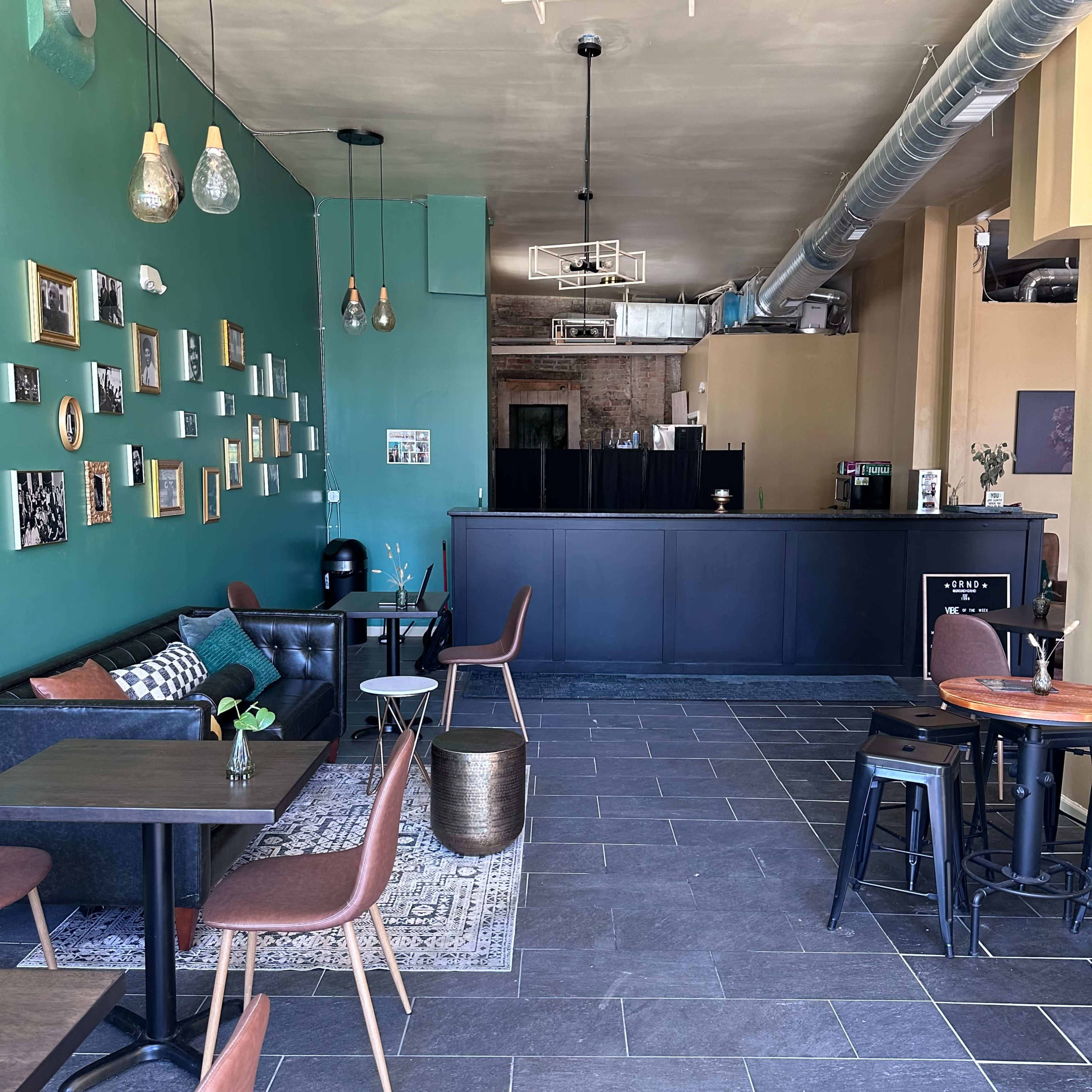 A cafe interior with green walls, a black counter, and a mix of seating options, including a leather sofa and metal chairs.