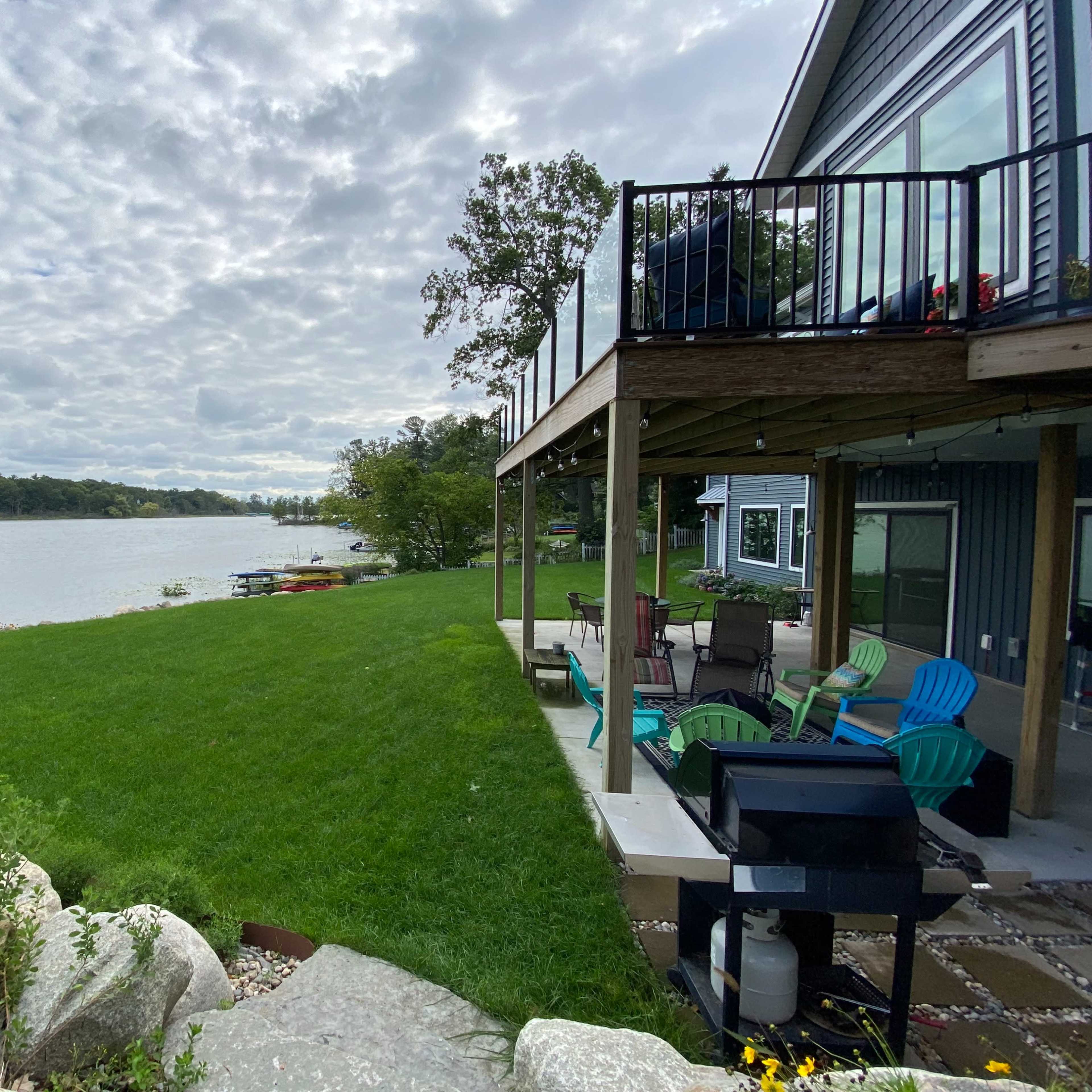A lakeside property with a grassy yard, a wooden deck, and colorful chairs overlooking the water.