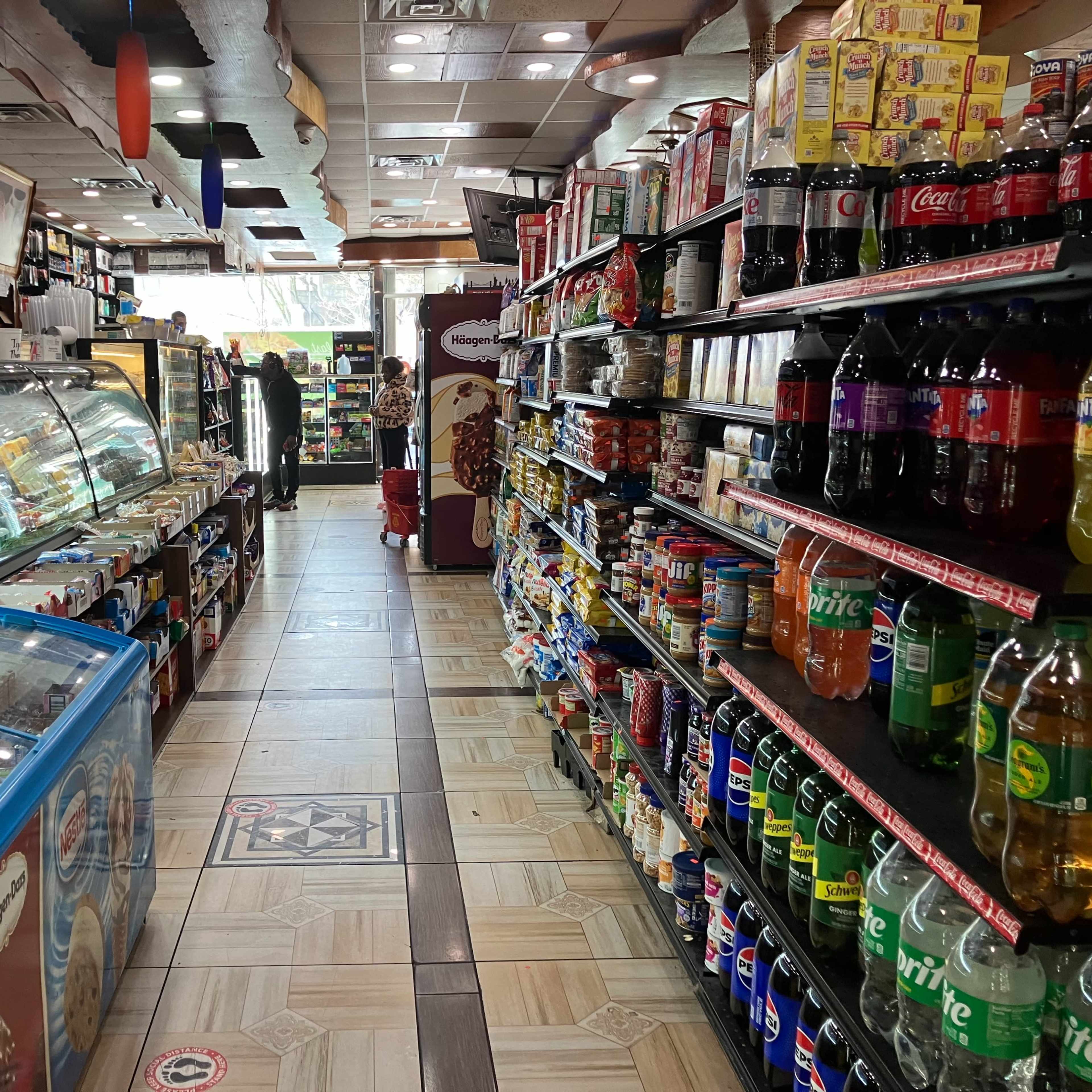 The interior of a convenience store with shelves stocked on both sides and a display case filled with food items at the front.