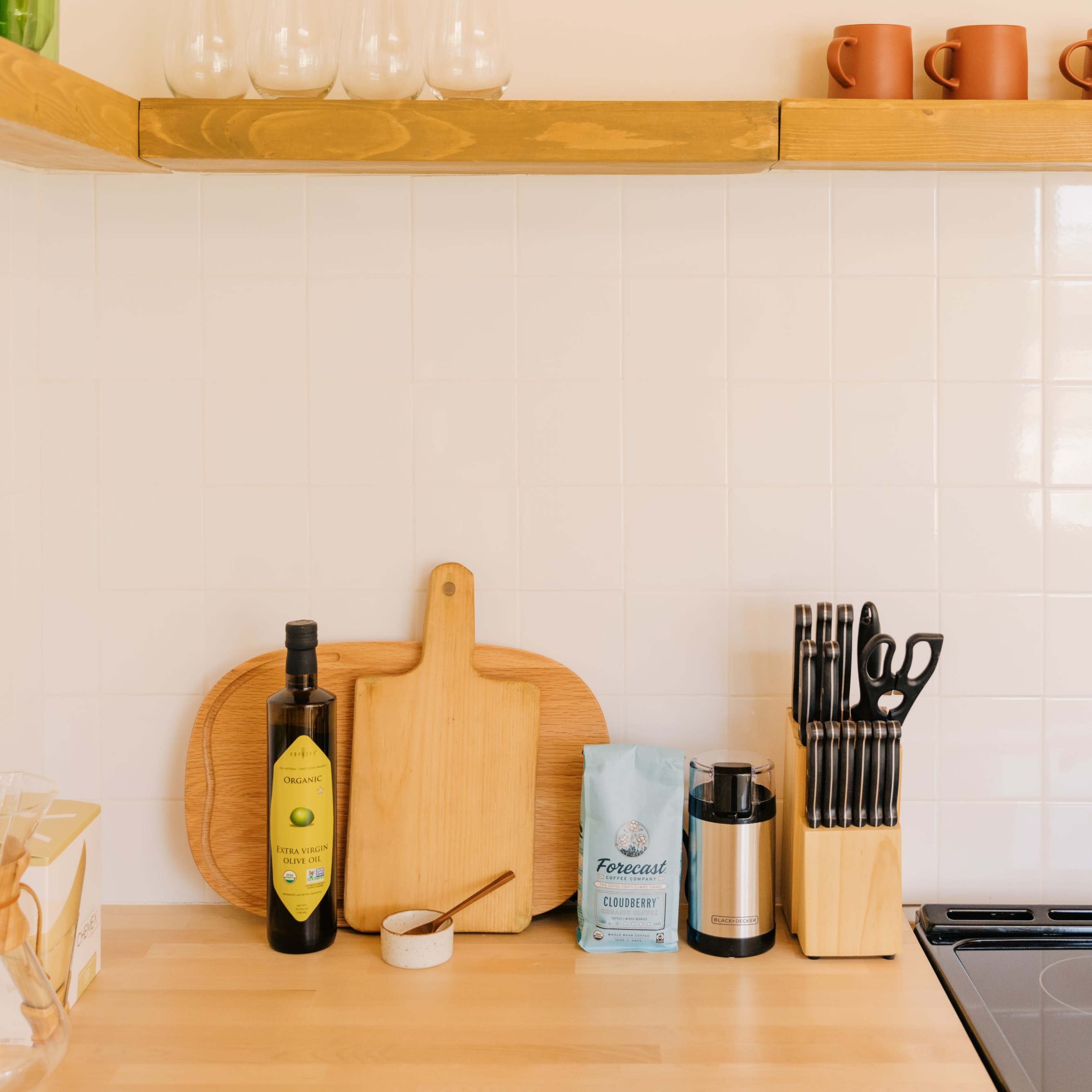 A kitchen countertop featuring wooden cutting boards, a bottle of olive oil, a container with utensils, and a packet of coffee beside a coffee grinder.