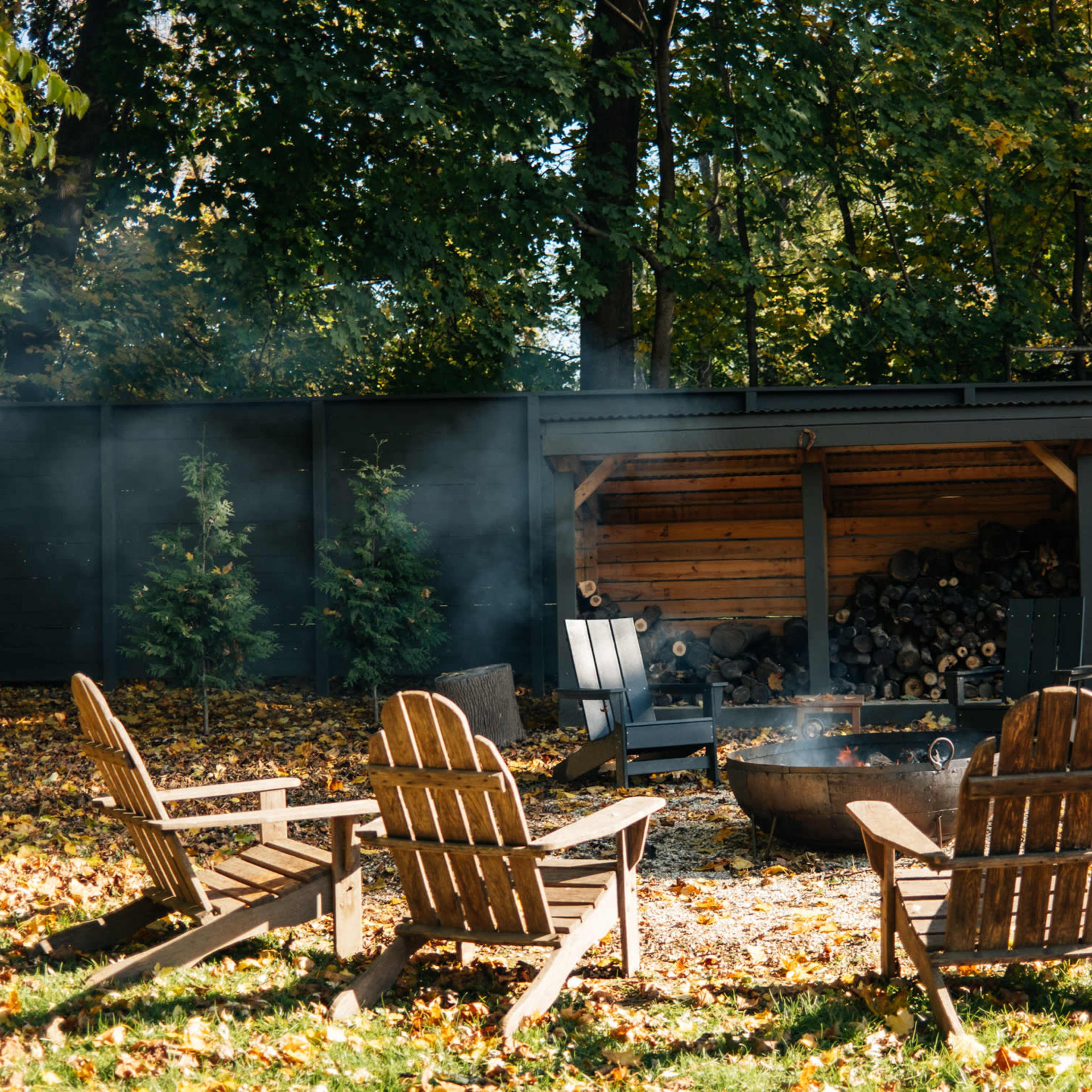 A circular arrangement of wooden chairs surrounds a fire pit in a forested outdoor setting.