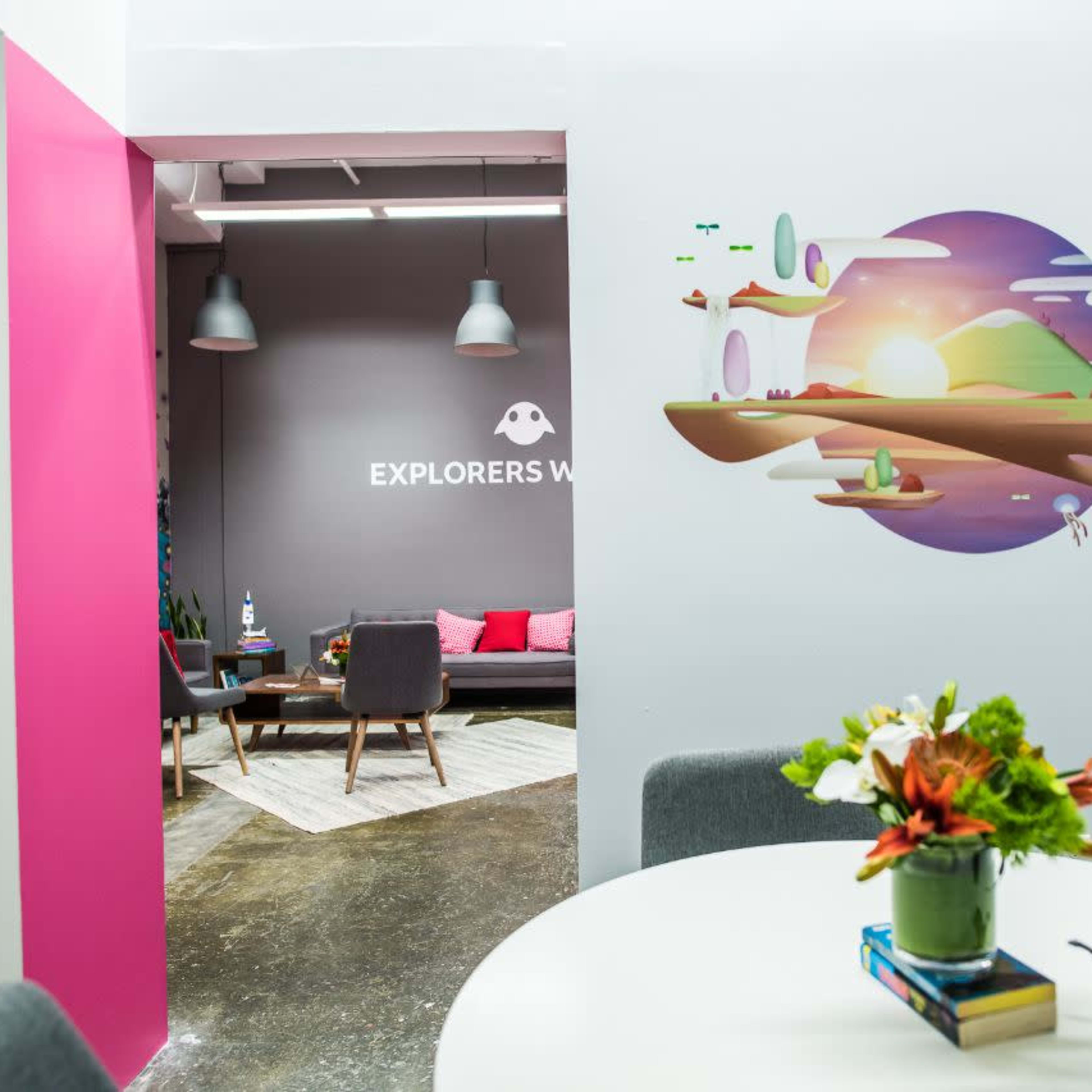A modern office space with a brightly colored wall featuring a whimsical mural and a view into a seating area with pink accents.