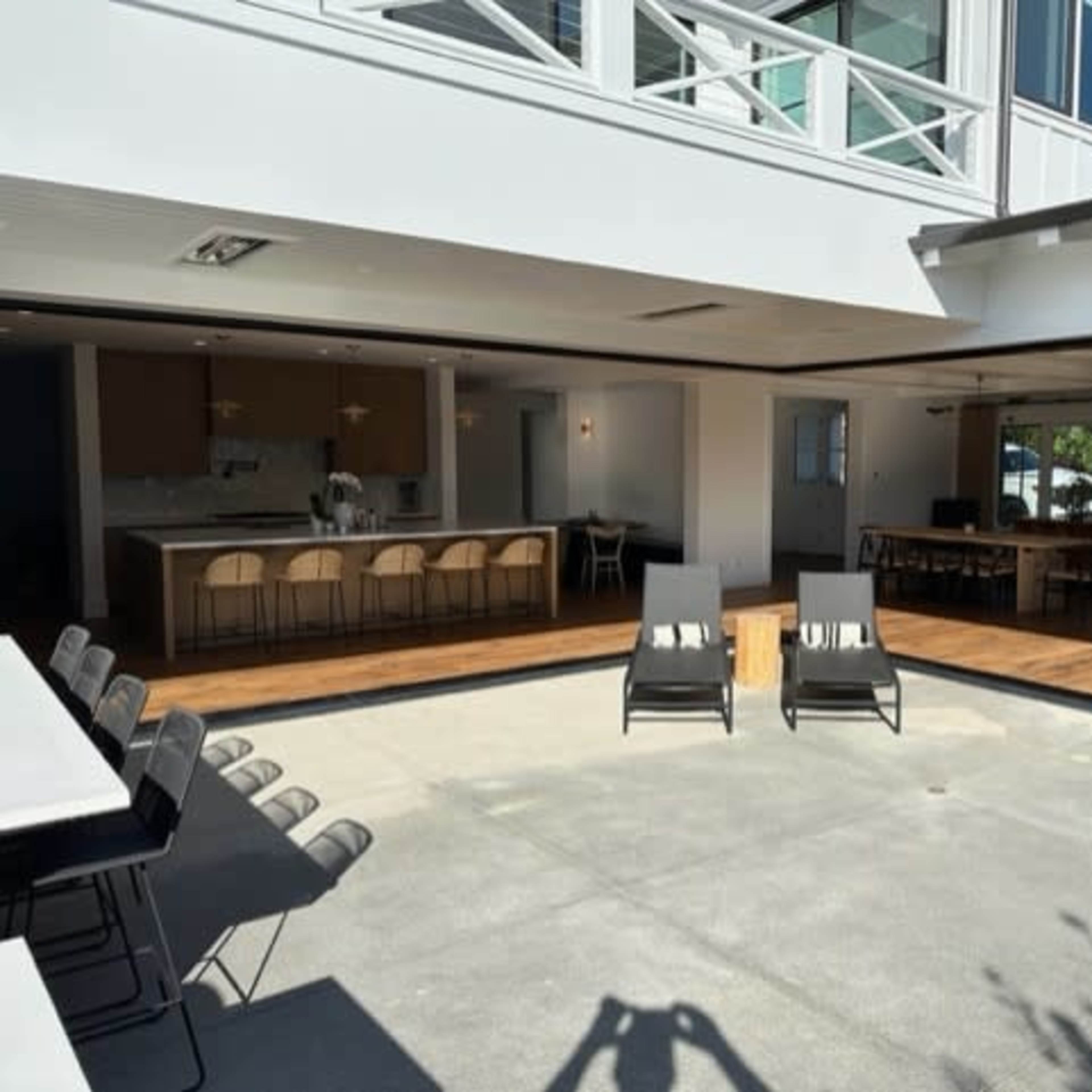 A spacious outdoor area featuring two lounge chairs, a central table, and an open layout connecting to a modern kitchen and dining space.