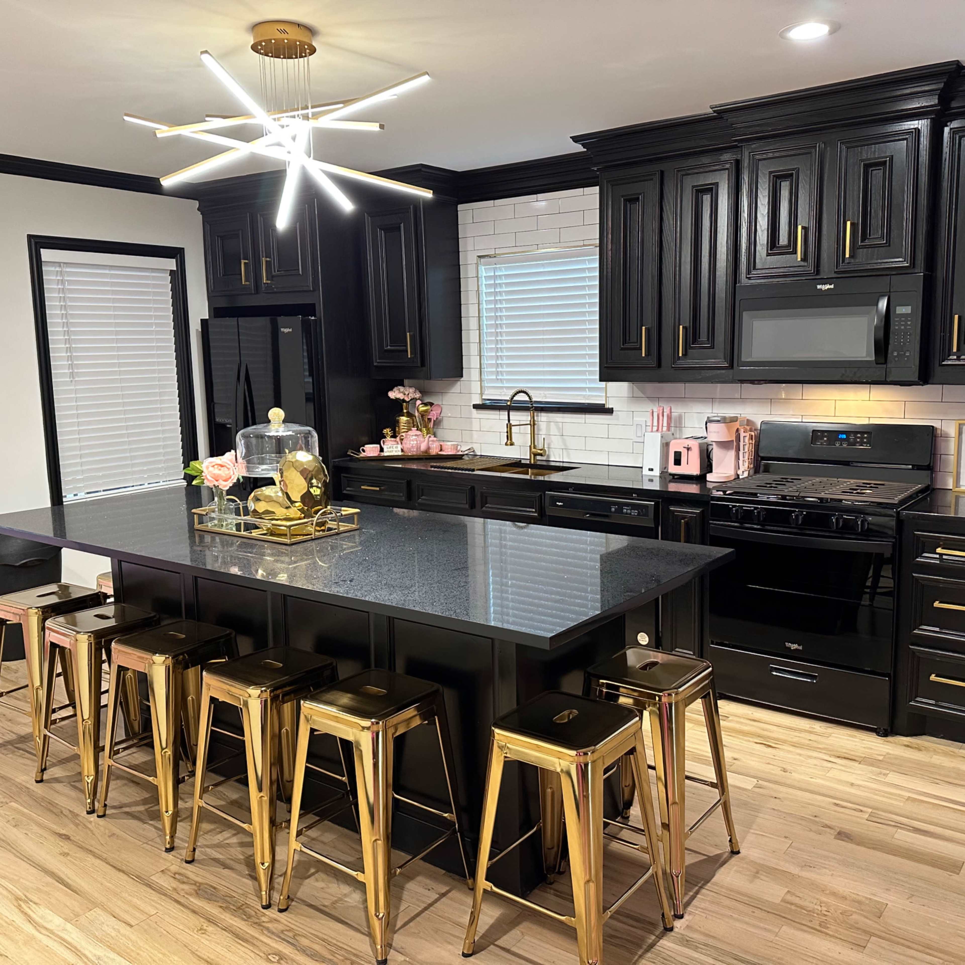 The modern kitchen features black cabinetry, a gold-accented island with seating, and a contemporary light fixture.