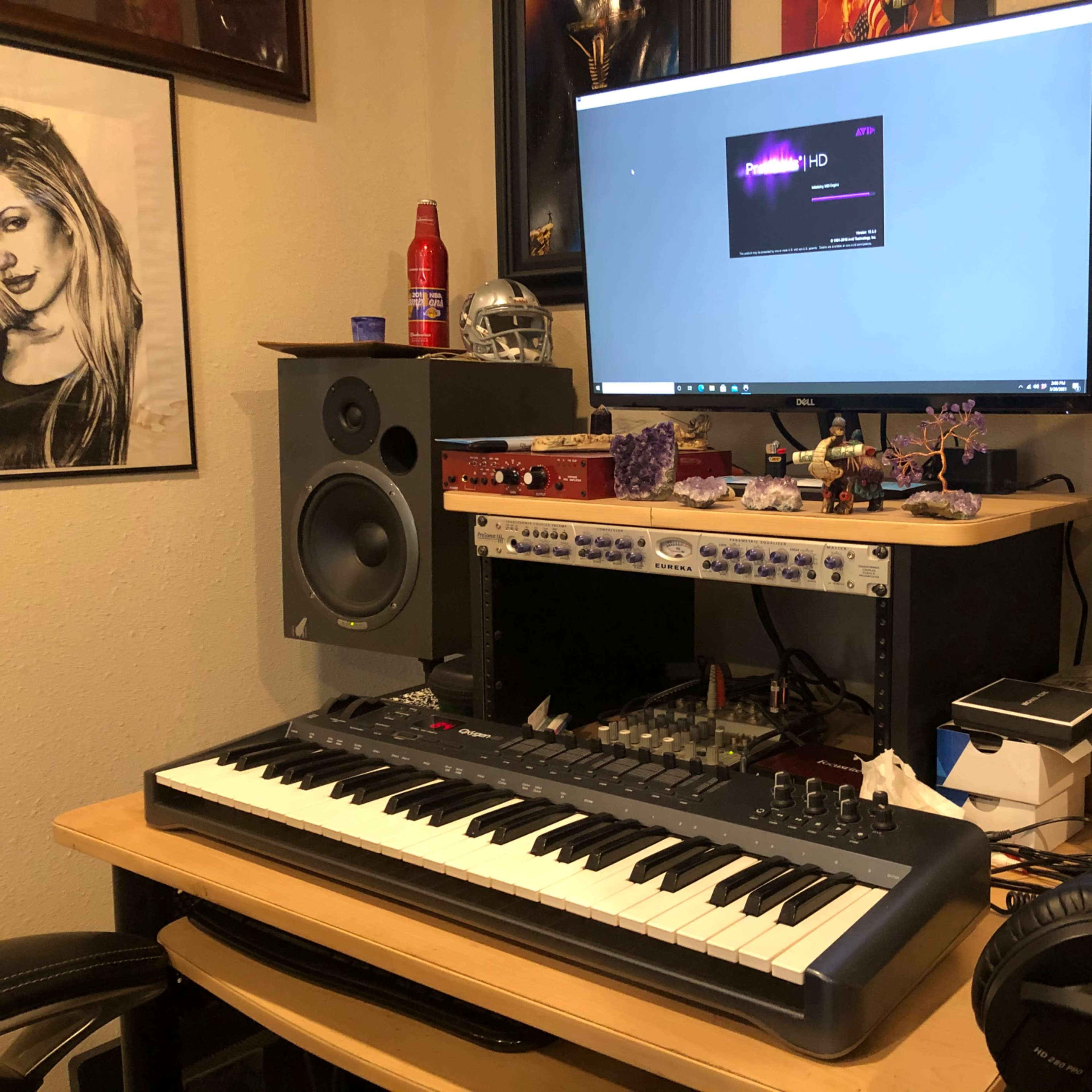 A music production setup is displayed, featuring a keyboard, computer monitor, audio interface, and studio monitors, along with decorative items on a desk.