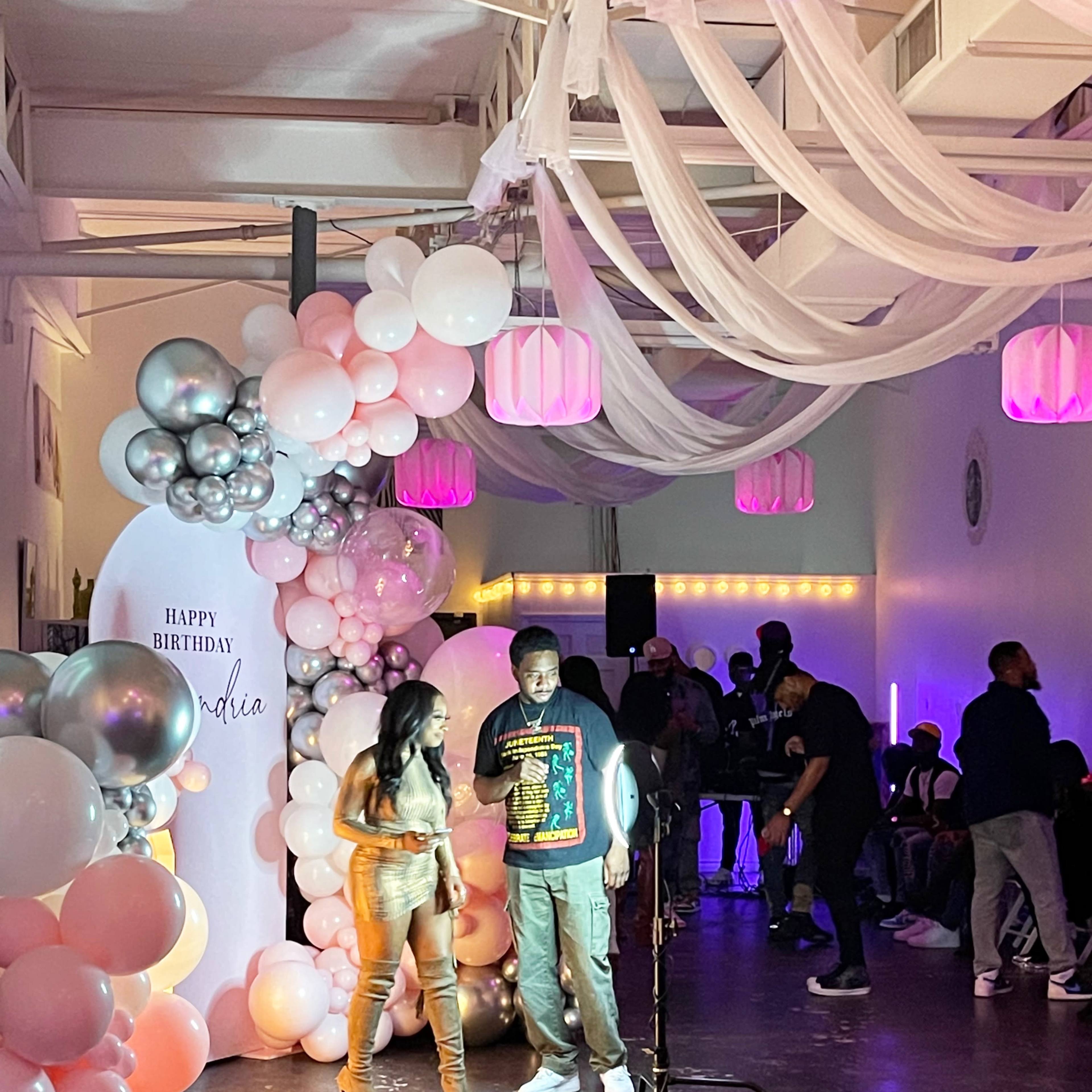A birthday party scene features pink and silver balloon decorations, a sign reading "Happy Birthday," and a DJ setup with guests mingling in the background.
