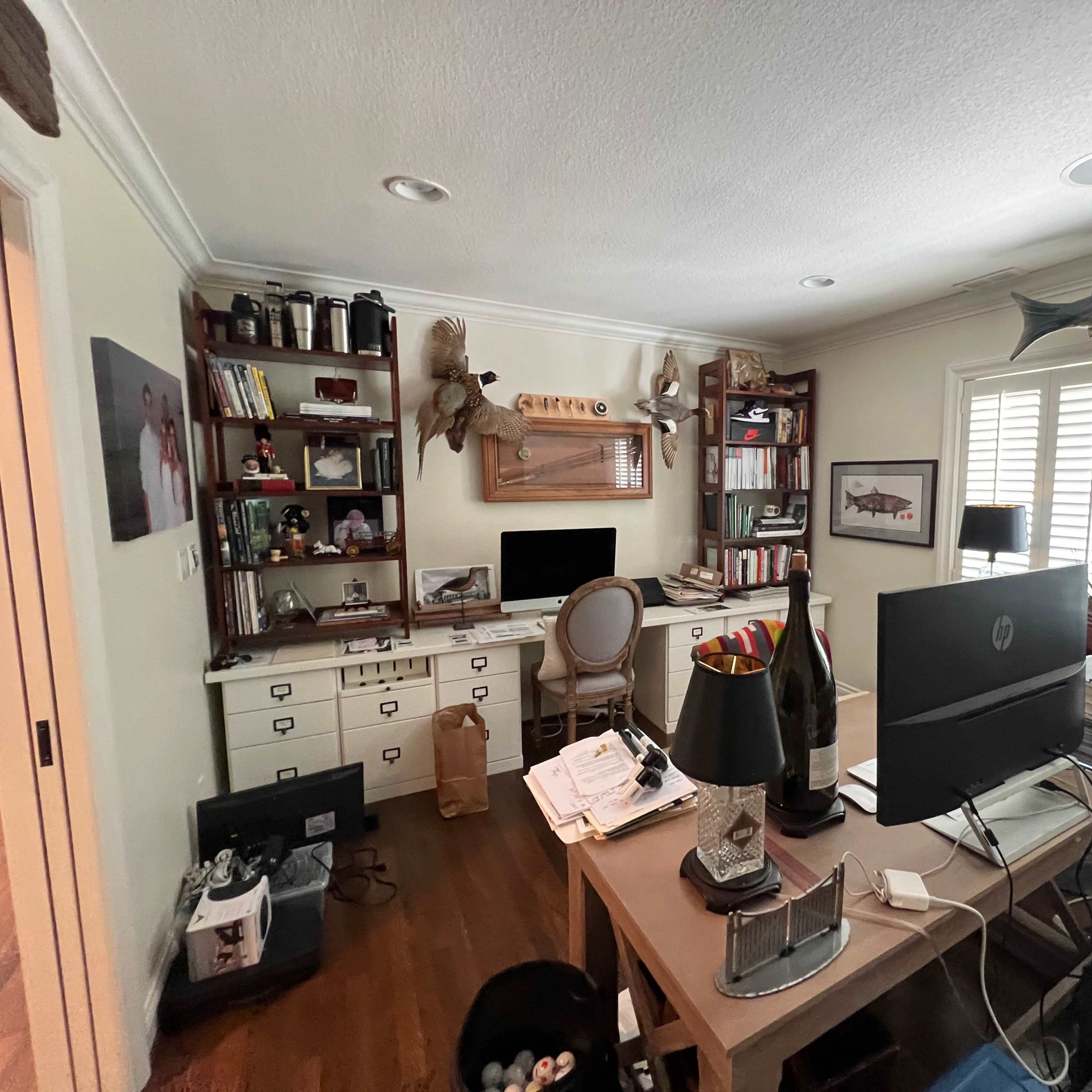 A home office with a desk, computer setup, bookshelves, and decorative fish on the walls.