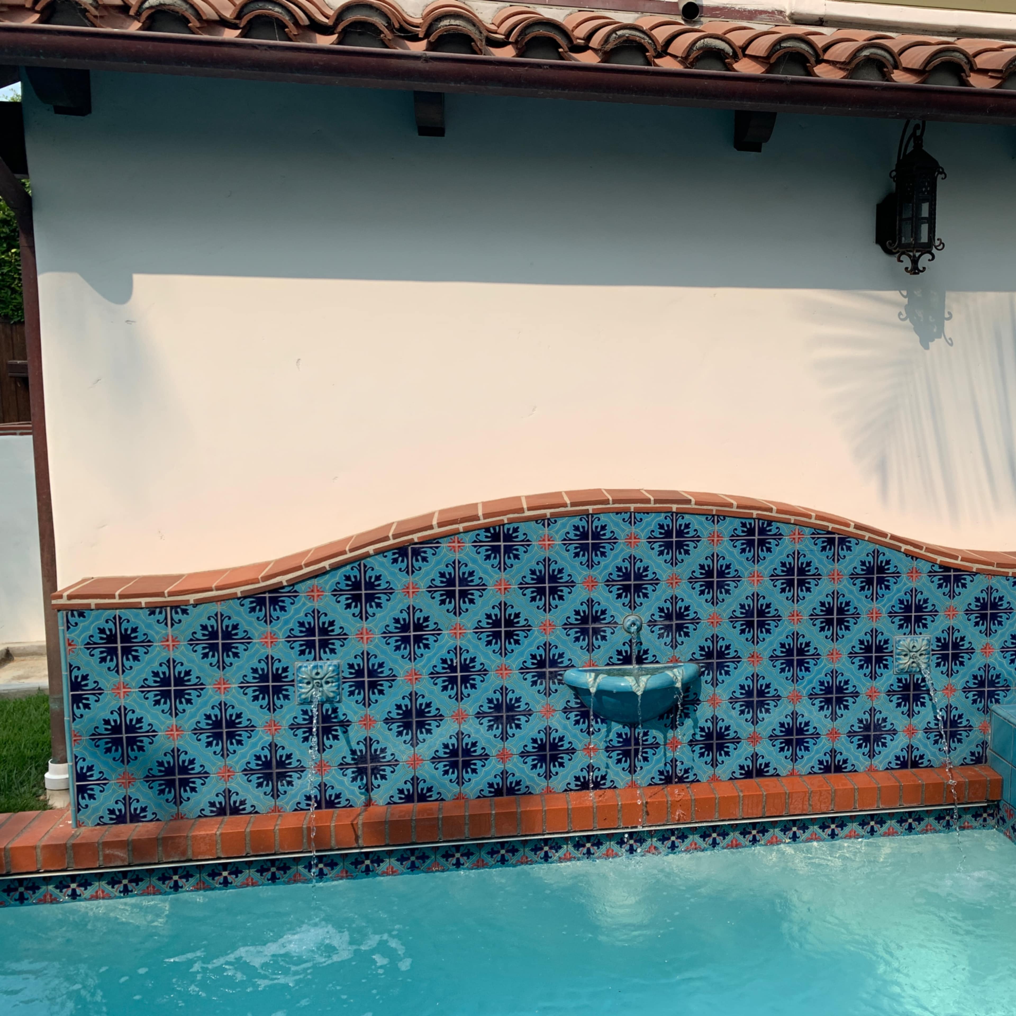 A decorative tiled fountain on a wall beside a swimming pool.