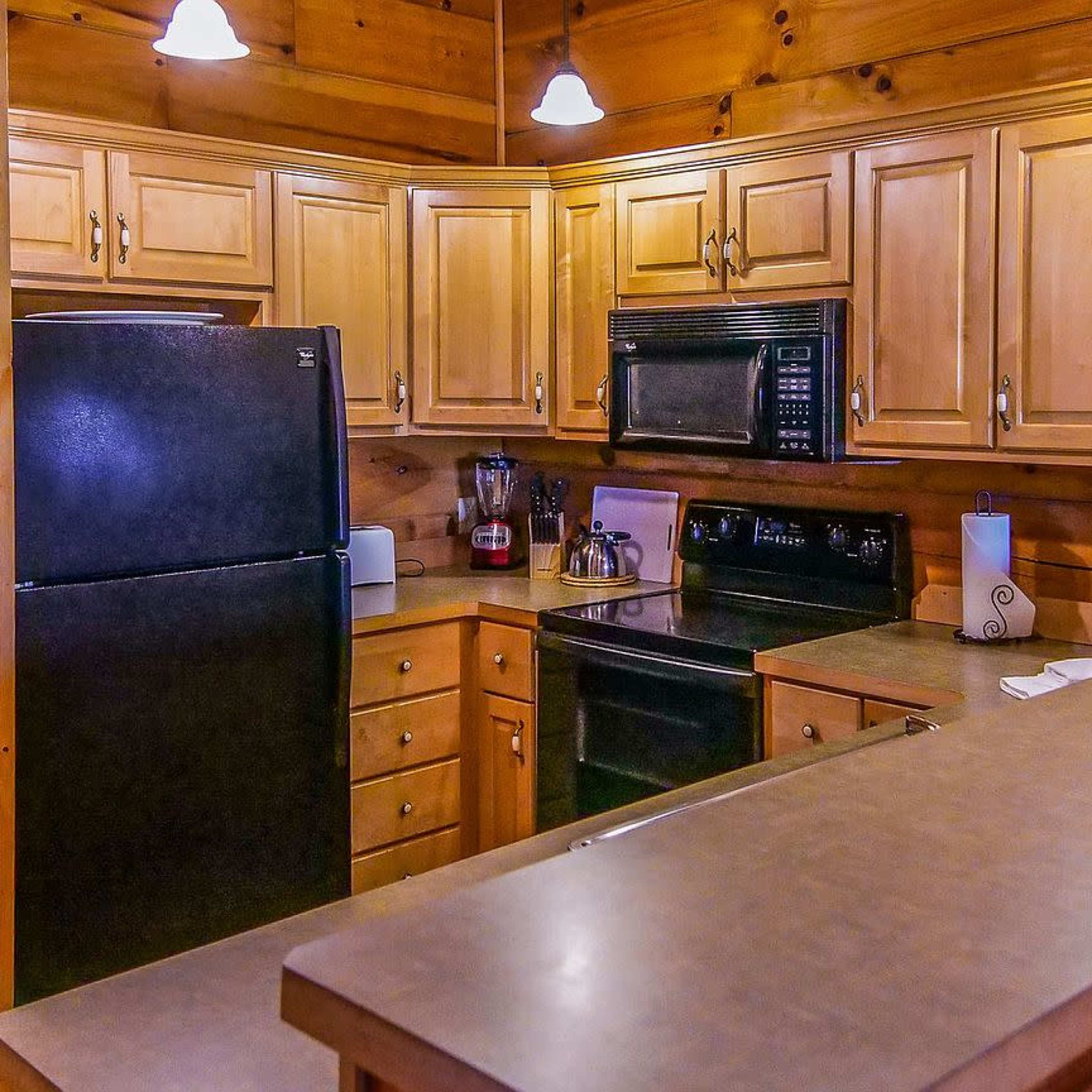 A wooden kitchen with light-colored cabinetry, a black refrigerator, and various kitchen appliances on a countertop.