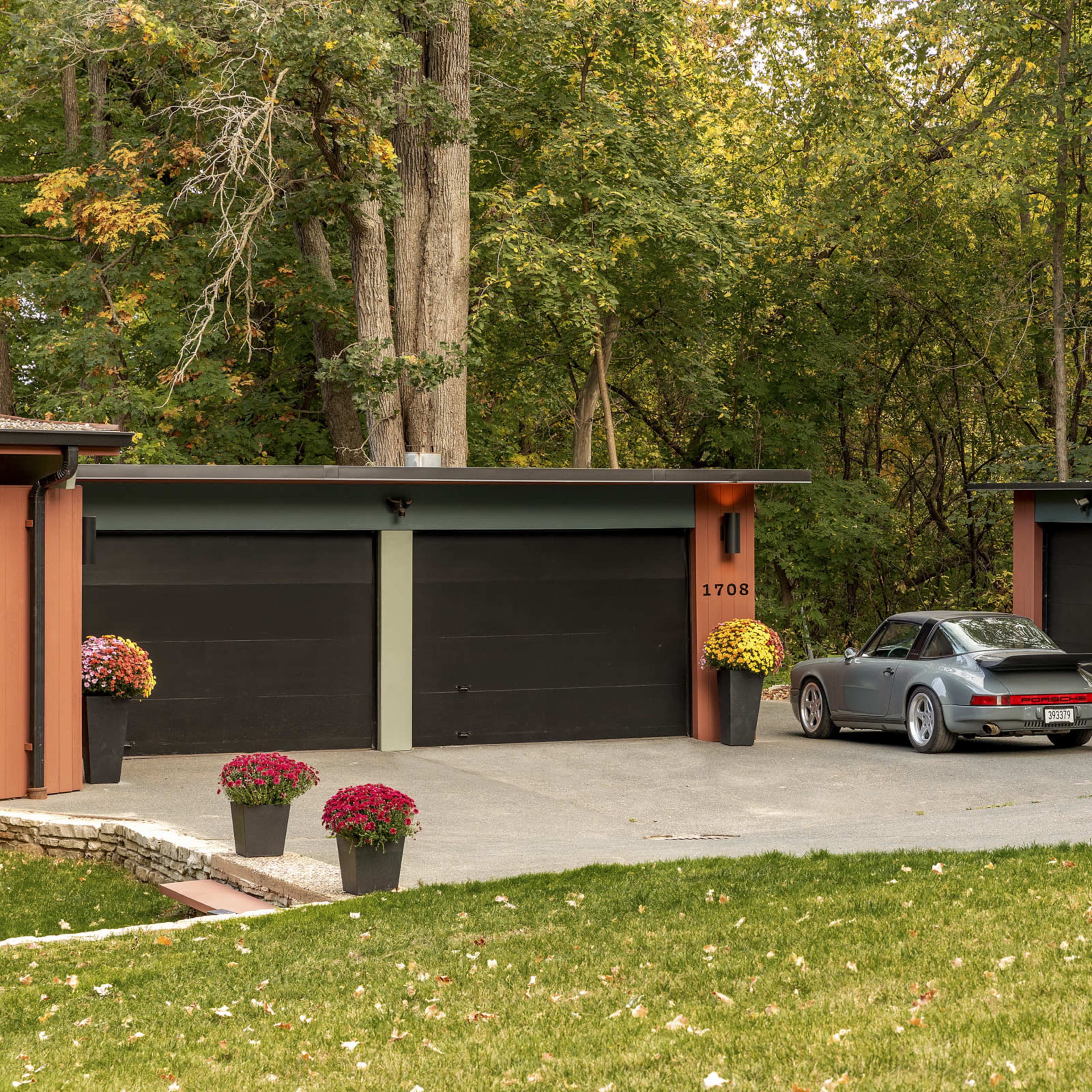 A modern home with a gray car parked in front of a two-car garage, surrounded by trees and flower pots.
