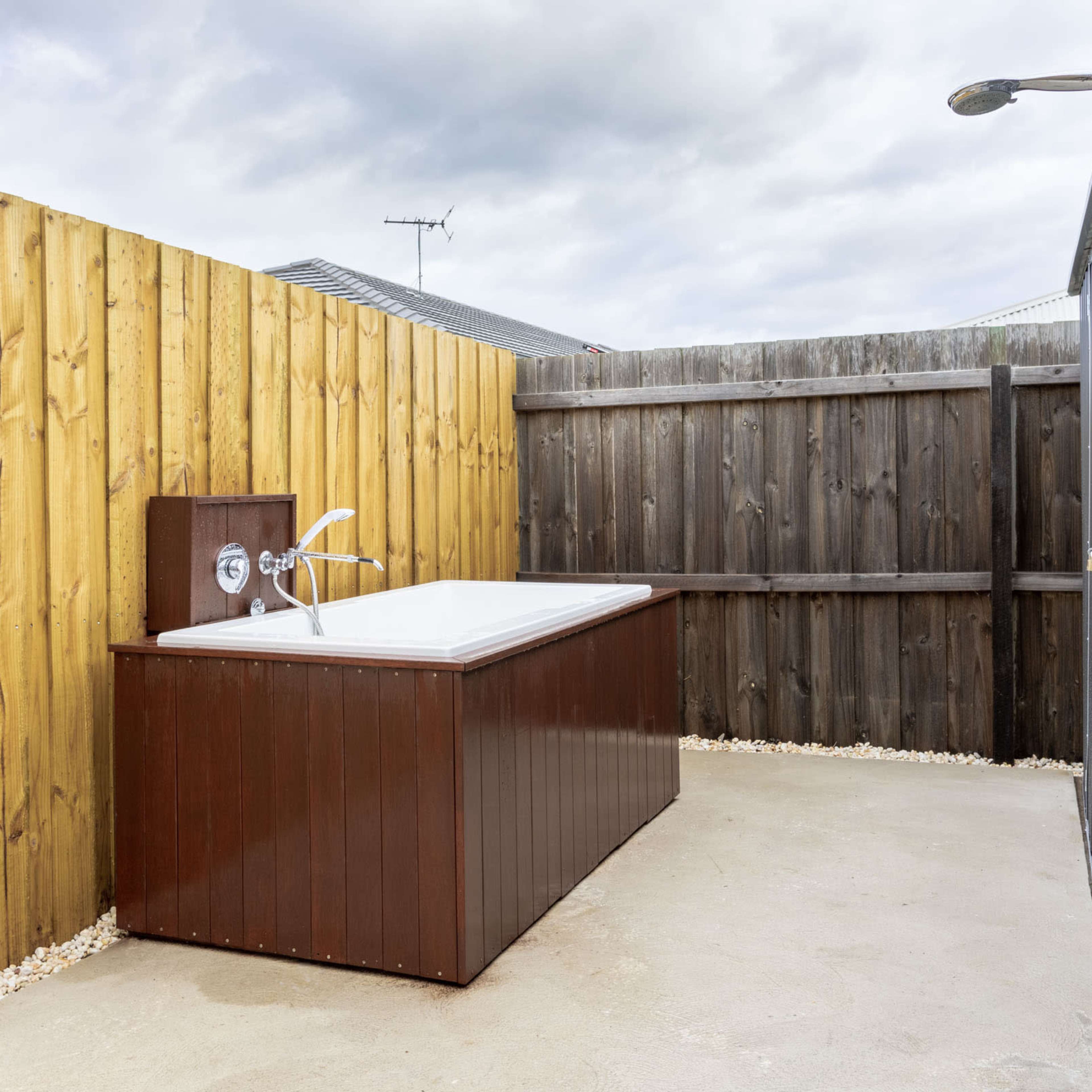 An outdoor area featuring a wooden-fenced space with a brown and white outdoor bathtub beside a shower fixture.