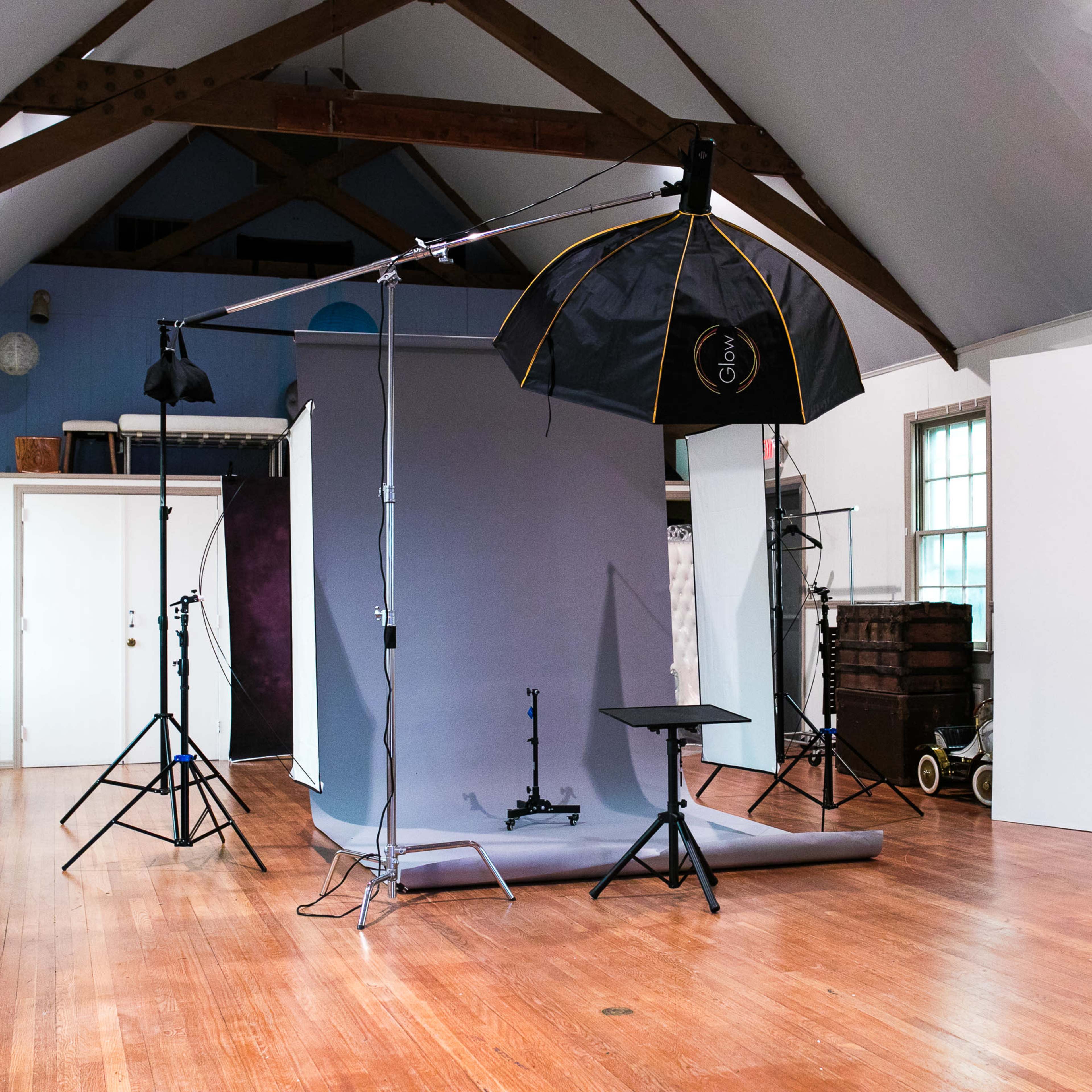 A photography studio with a backdrop, lighting equipment, and empty spaces around a wooden floor.
