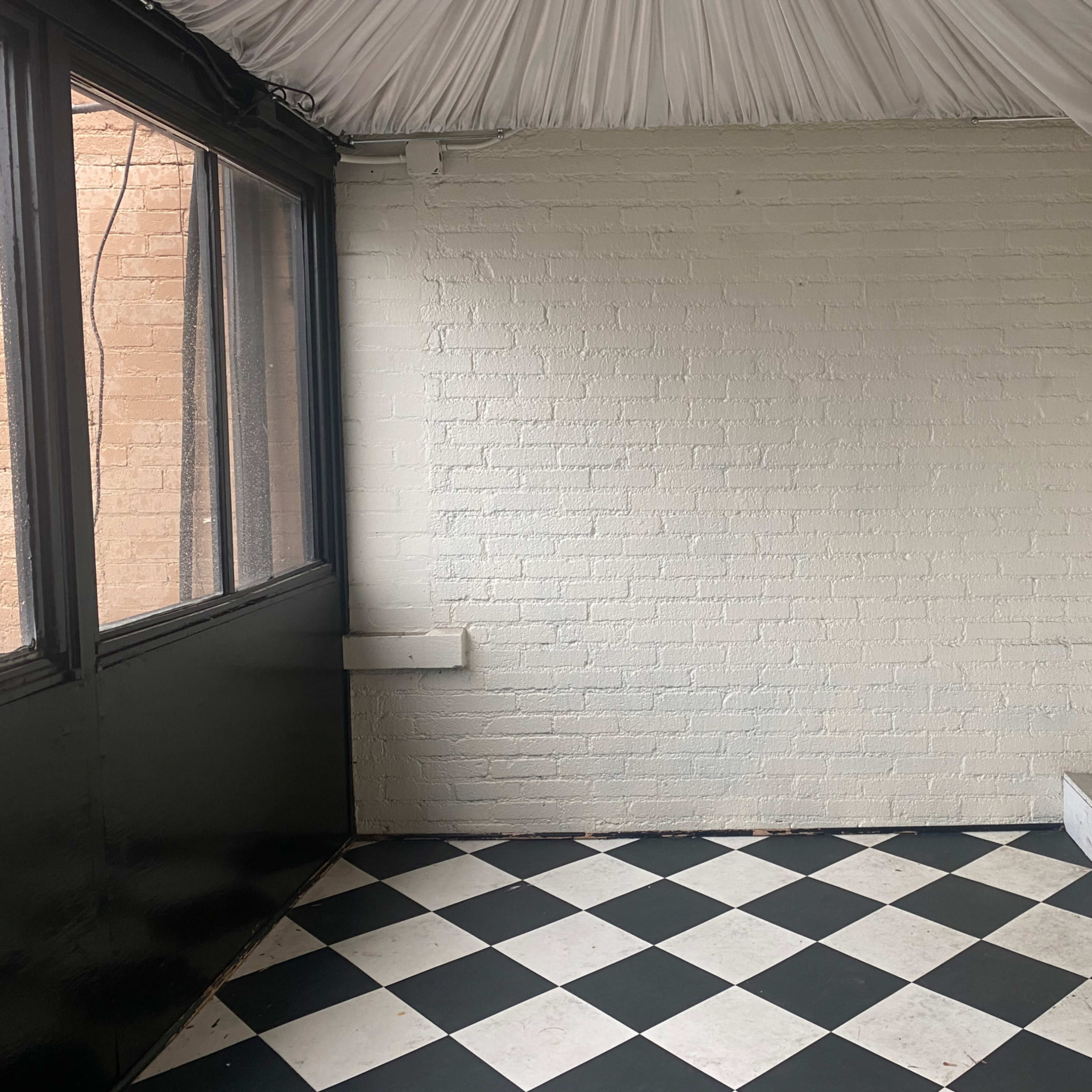 An empty room with a checkered black and white floor, white brick walls, and a door at the far end.