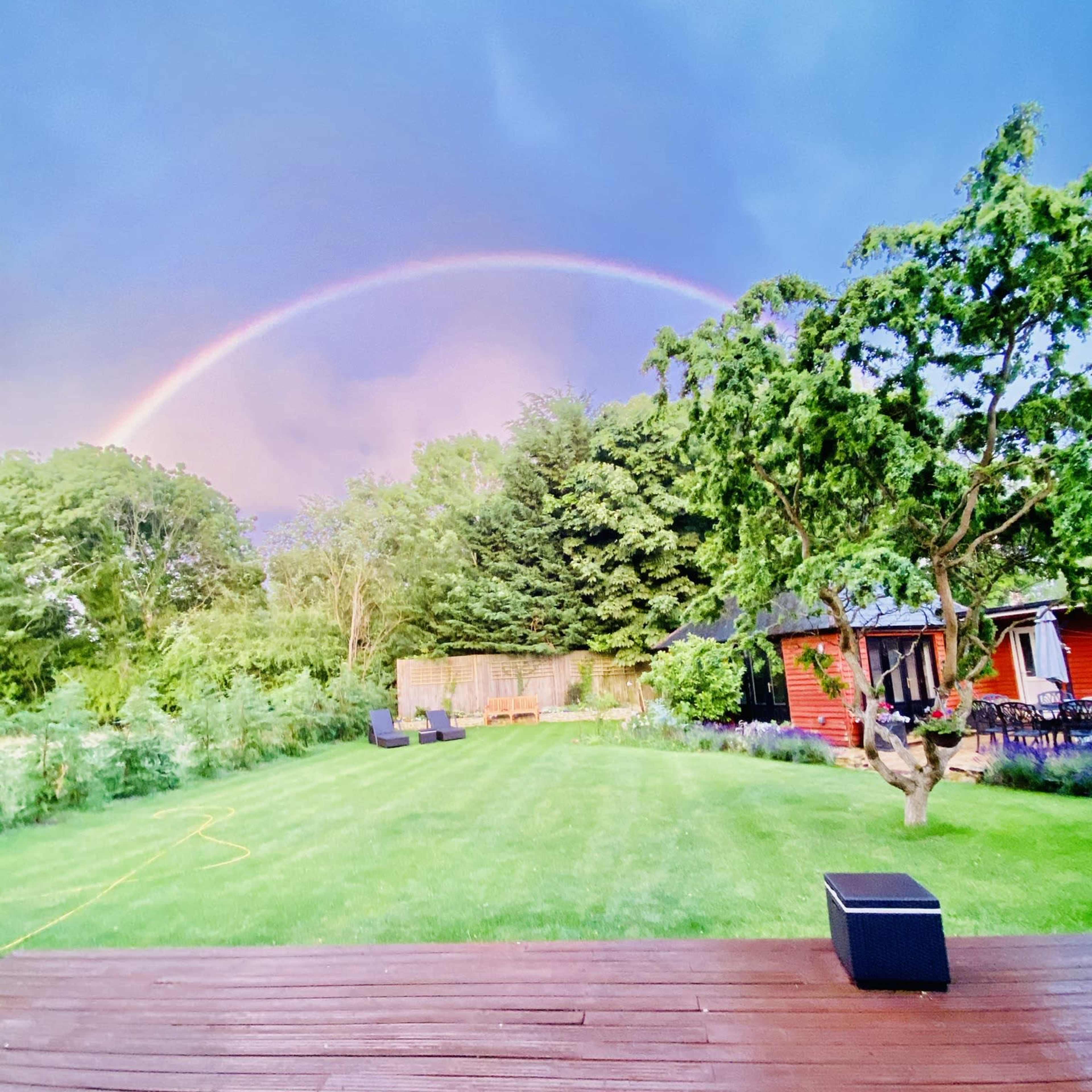 A wooden deck overlooks a lush green lawn with a rainbow arching through a cloudy sky in the background.