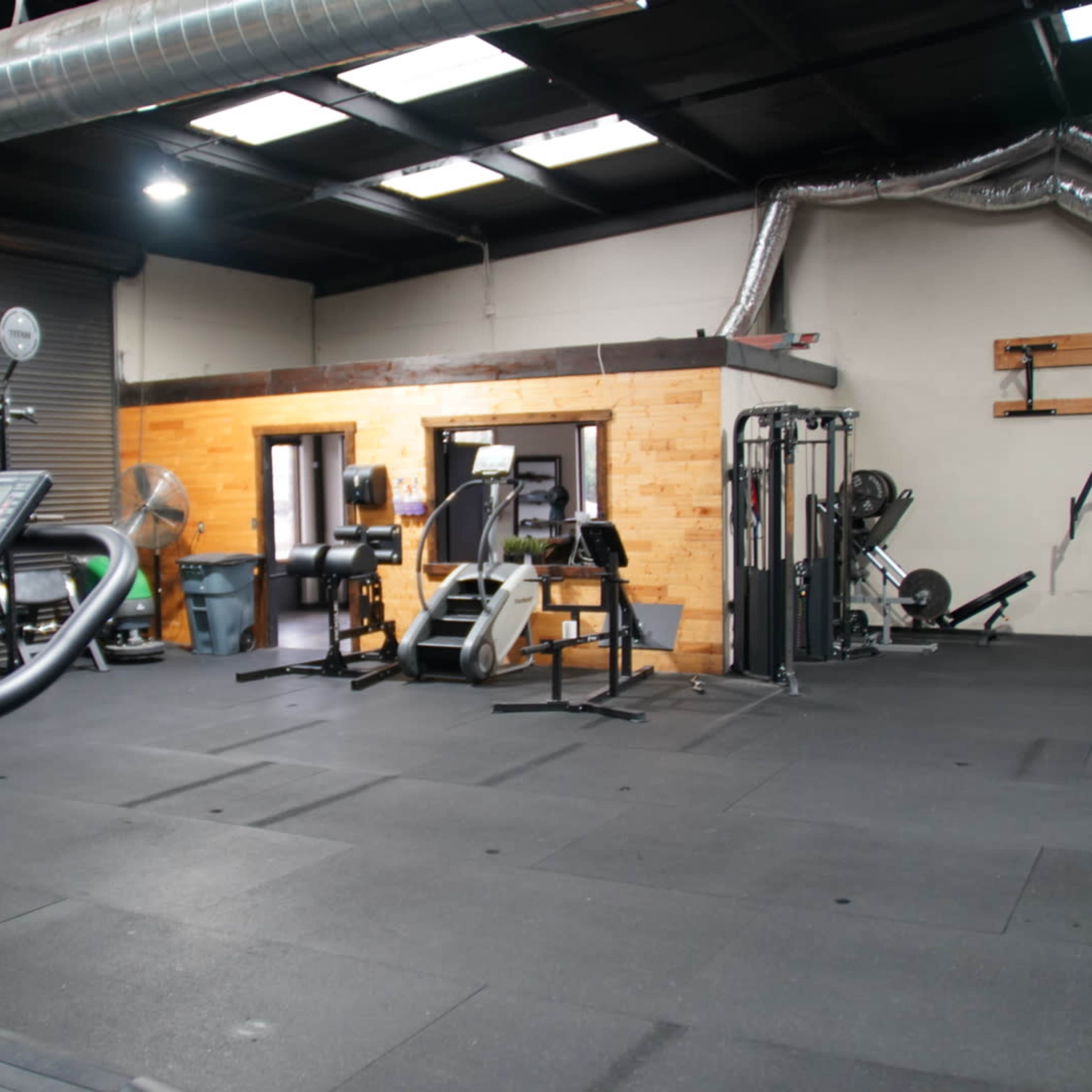 A gym interior with various exercise equipment and individuals working out in a spacious area.