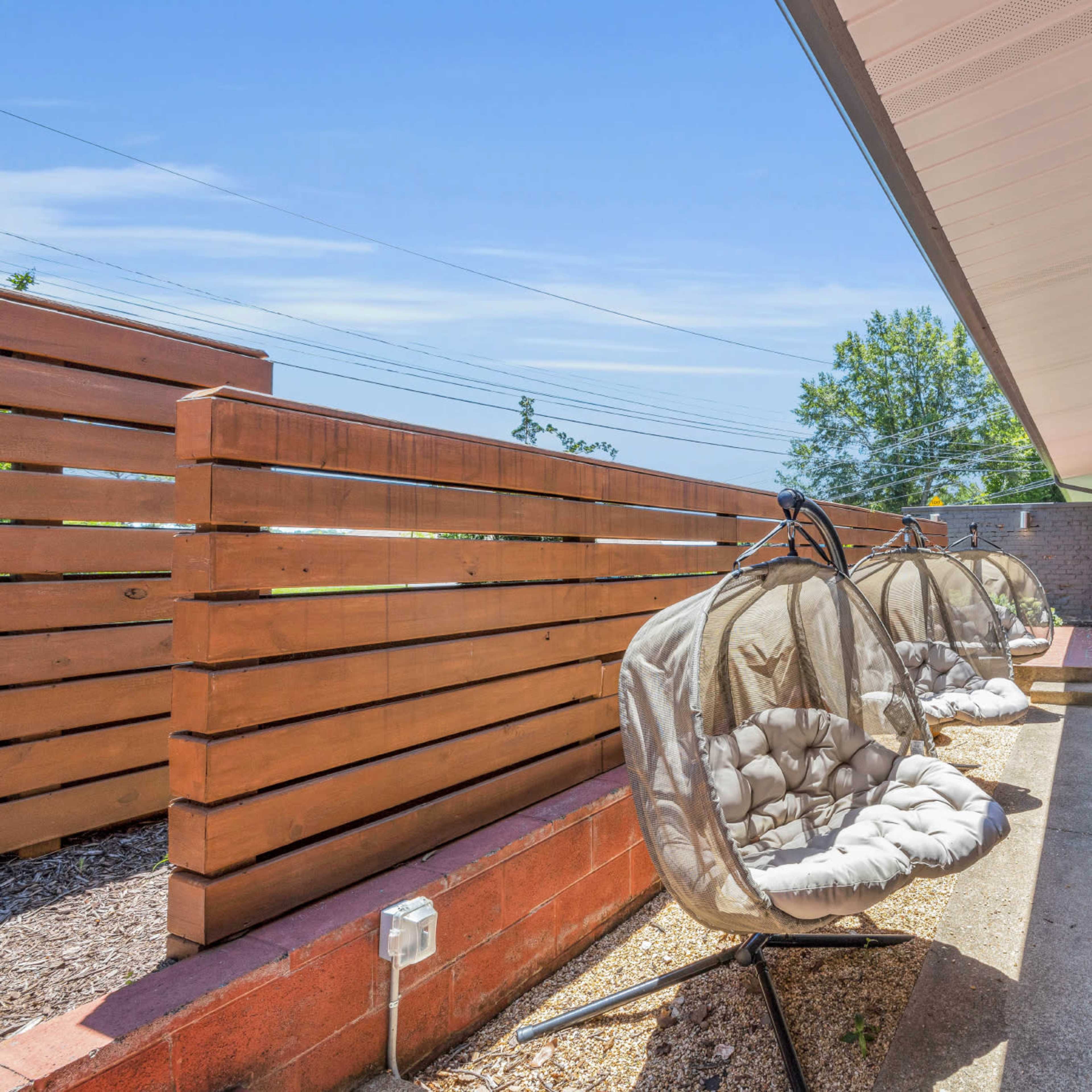 A row of suspended chairs are set on a concrete patio beside a wall of wood paneling.