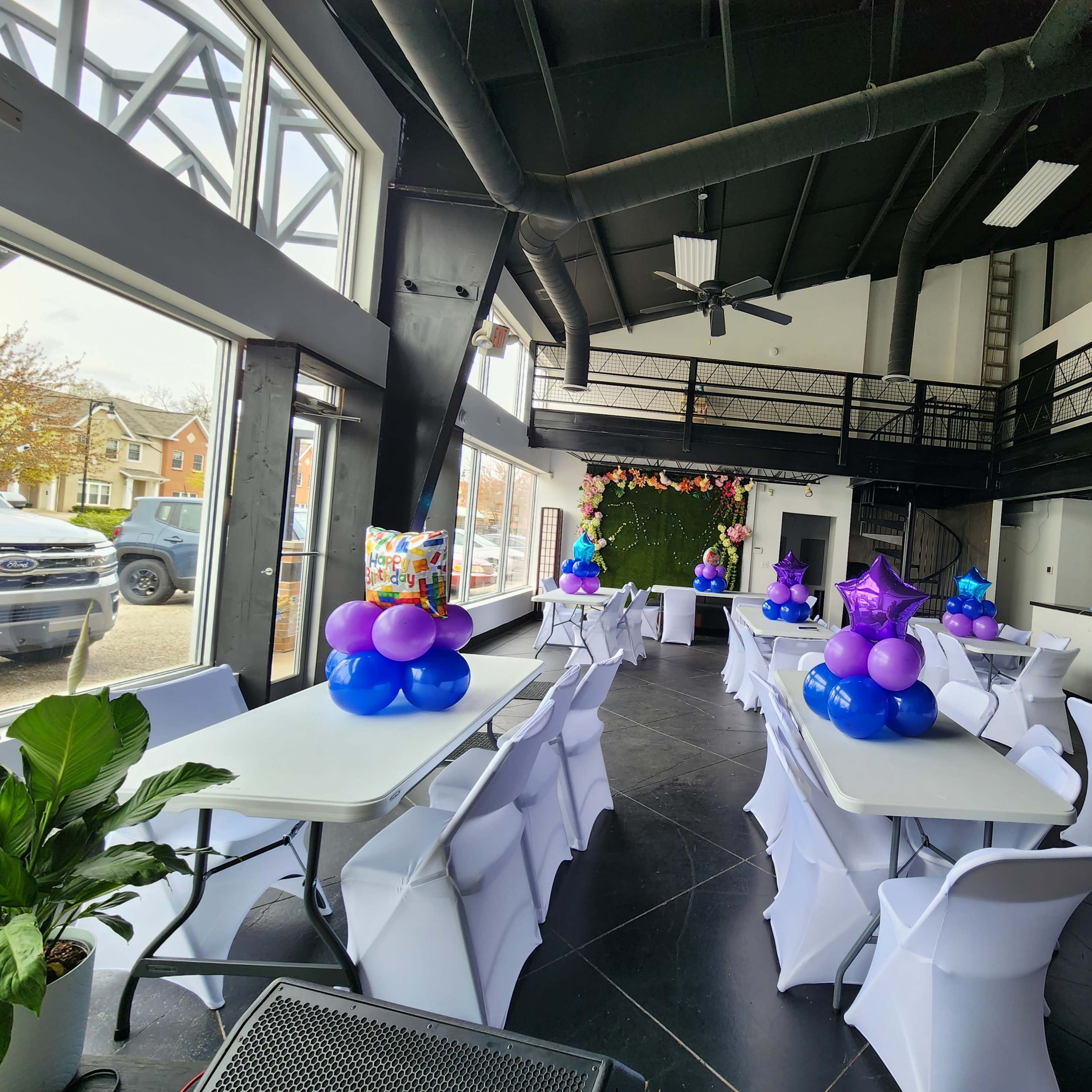 A modern event space with white tables decorated with blue and purple balloons, arranged for a gathering.