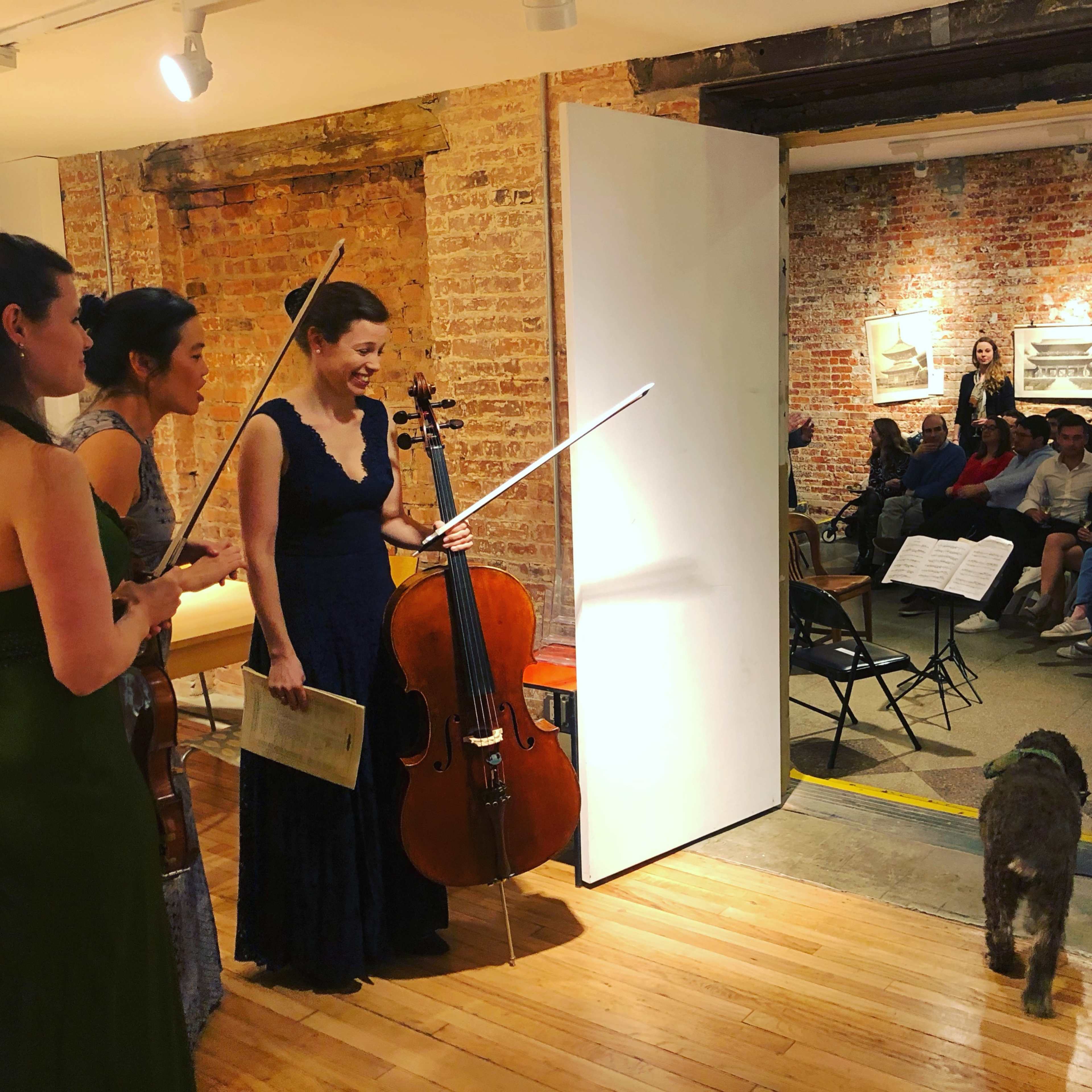 A string quartet performs in a gallery space while an audience seated in rows listens attentively.
