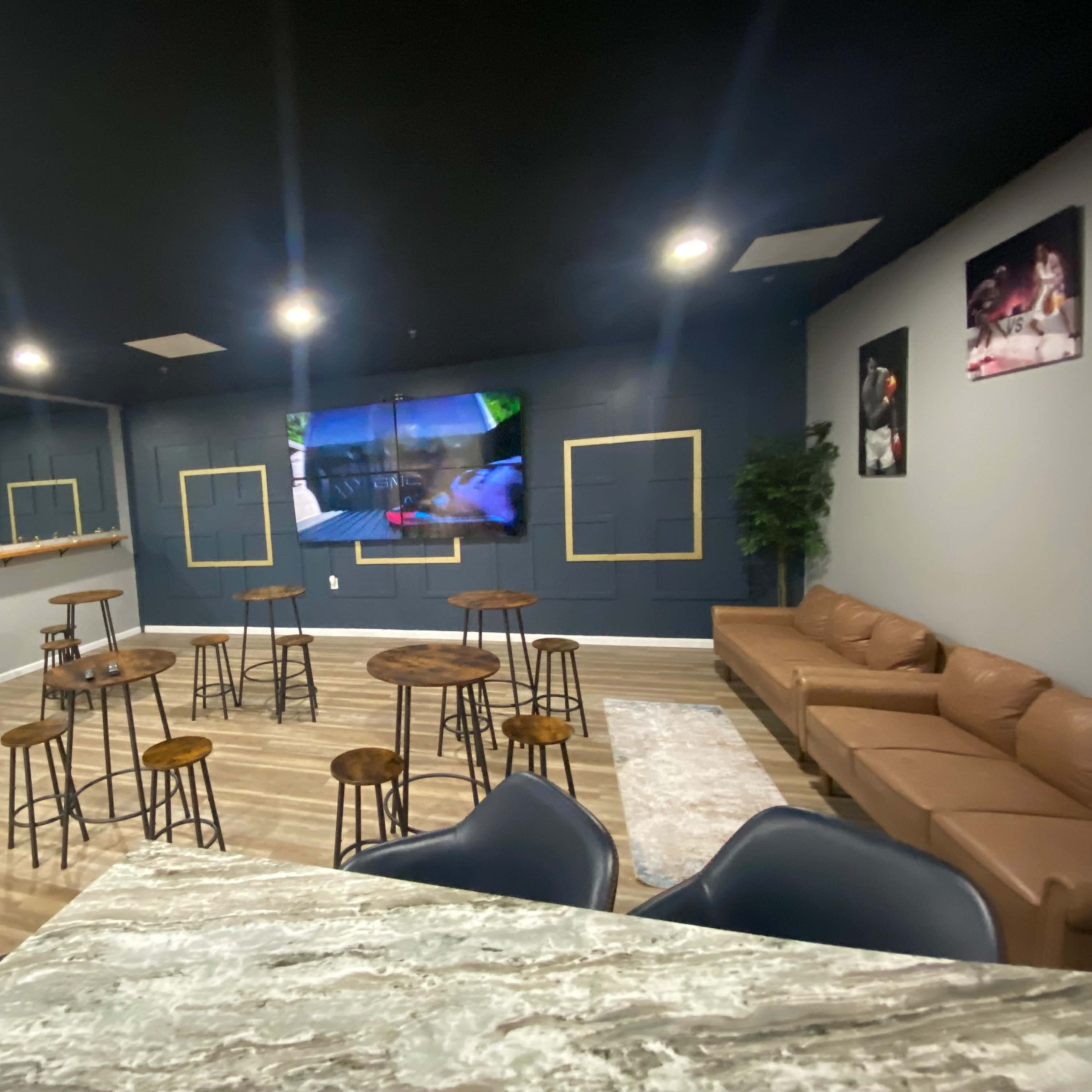 A modern lounge area with a stone accent wall, several wooden tables and stools, a brown sofa, and multiple screens displaying content on the walls.