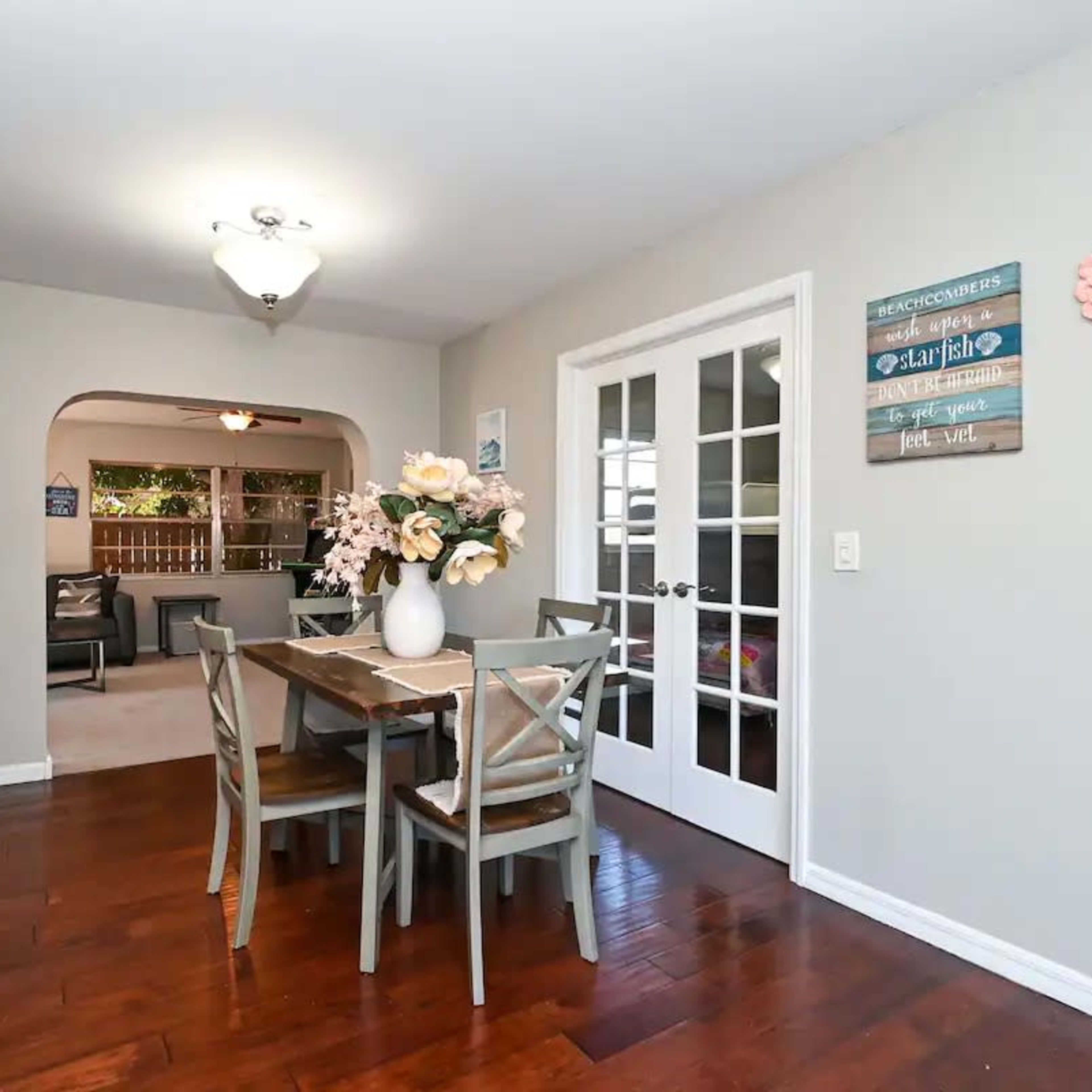 A dining area features a wooden table with chairs, a floral centerpiece, and a doorway leading to another room.