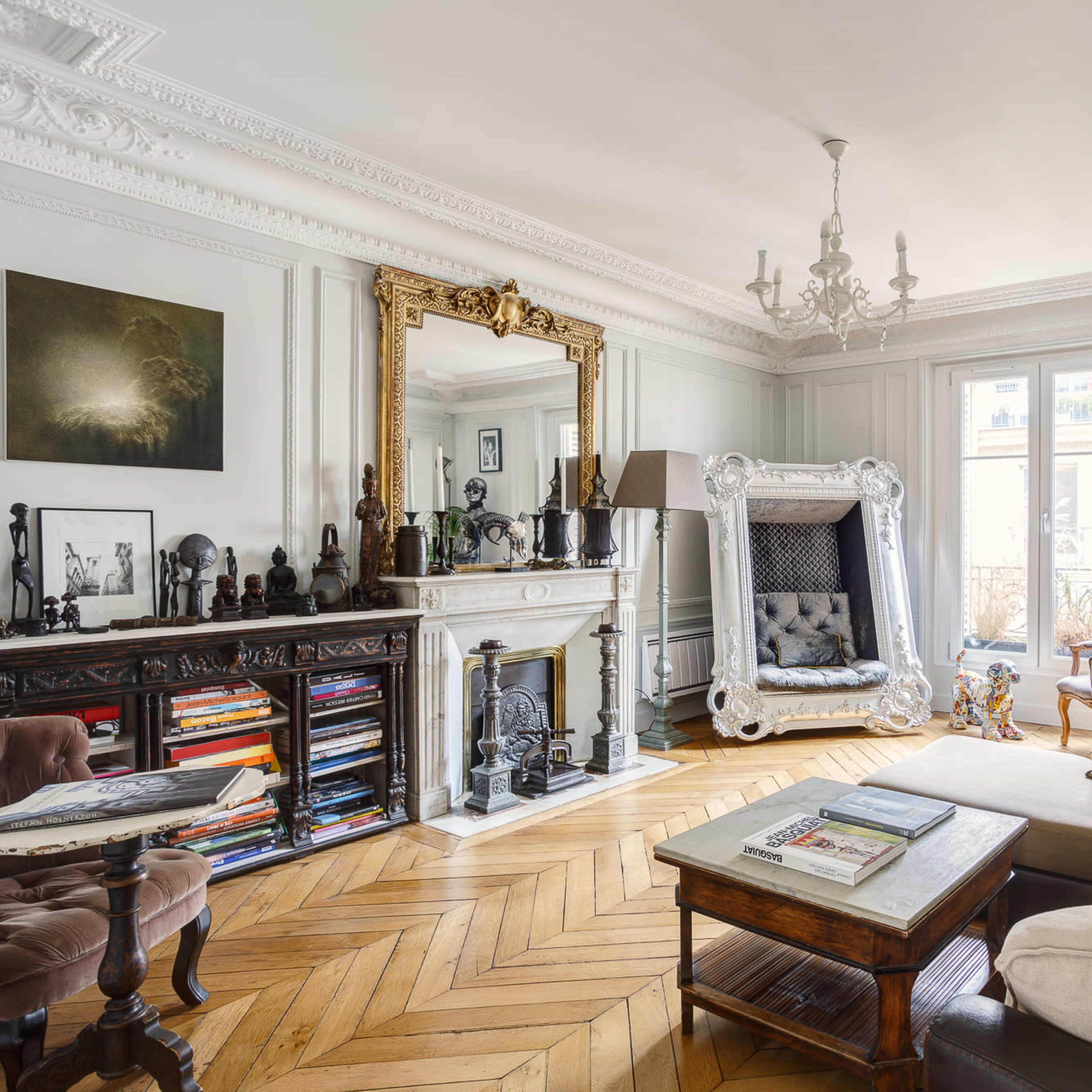 A stylish living room with a white couch, hardwood flooring, ornate molding, and decorative furnishings including a large mirror and various sculptures.
