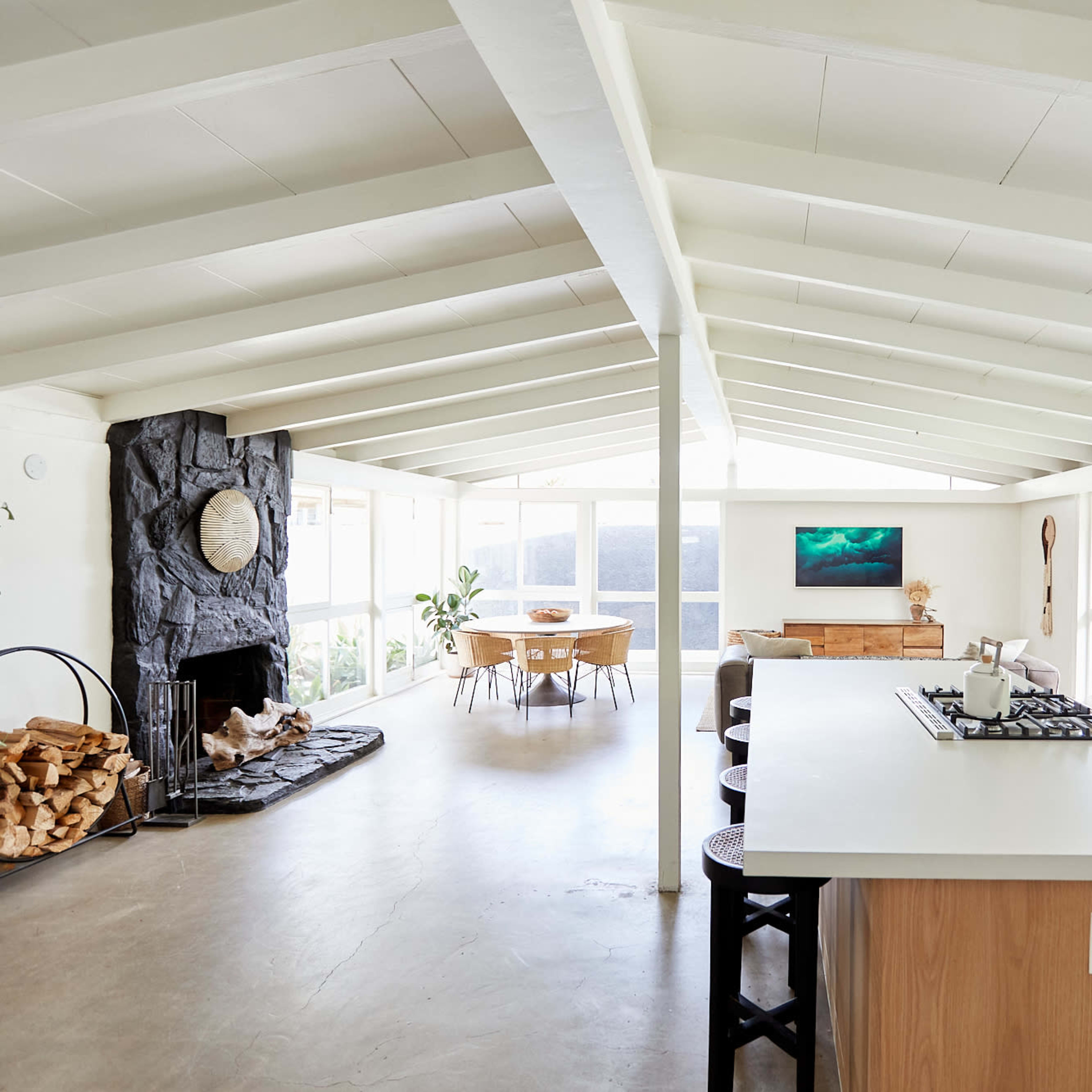 A modern, open-concept kitchen and living area with a stone fireplace, large windows, and a dining table.