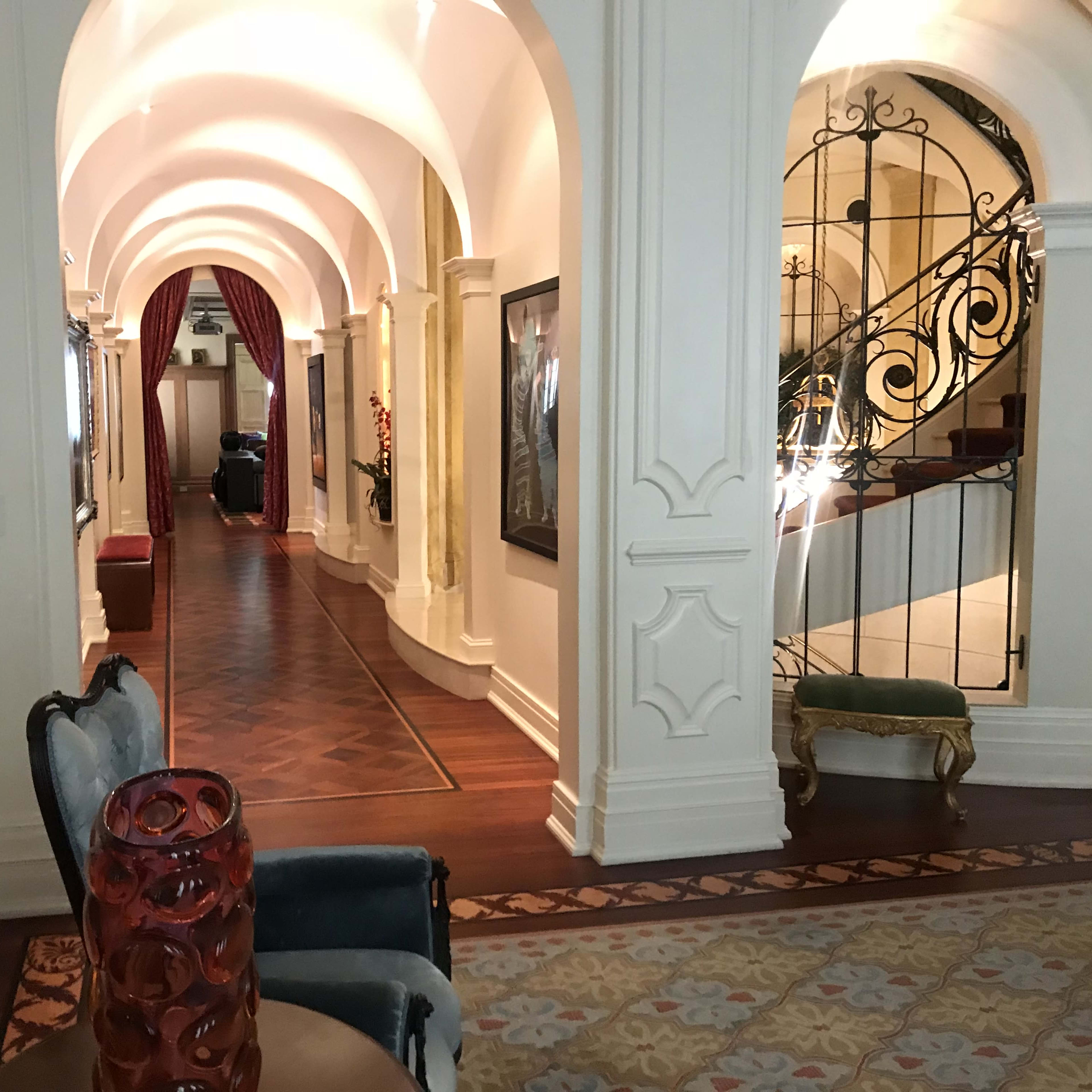 A long hallway with arched ceilings, decorative wall moldings, and wooden flooring, leading to a staircase.