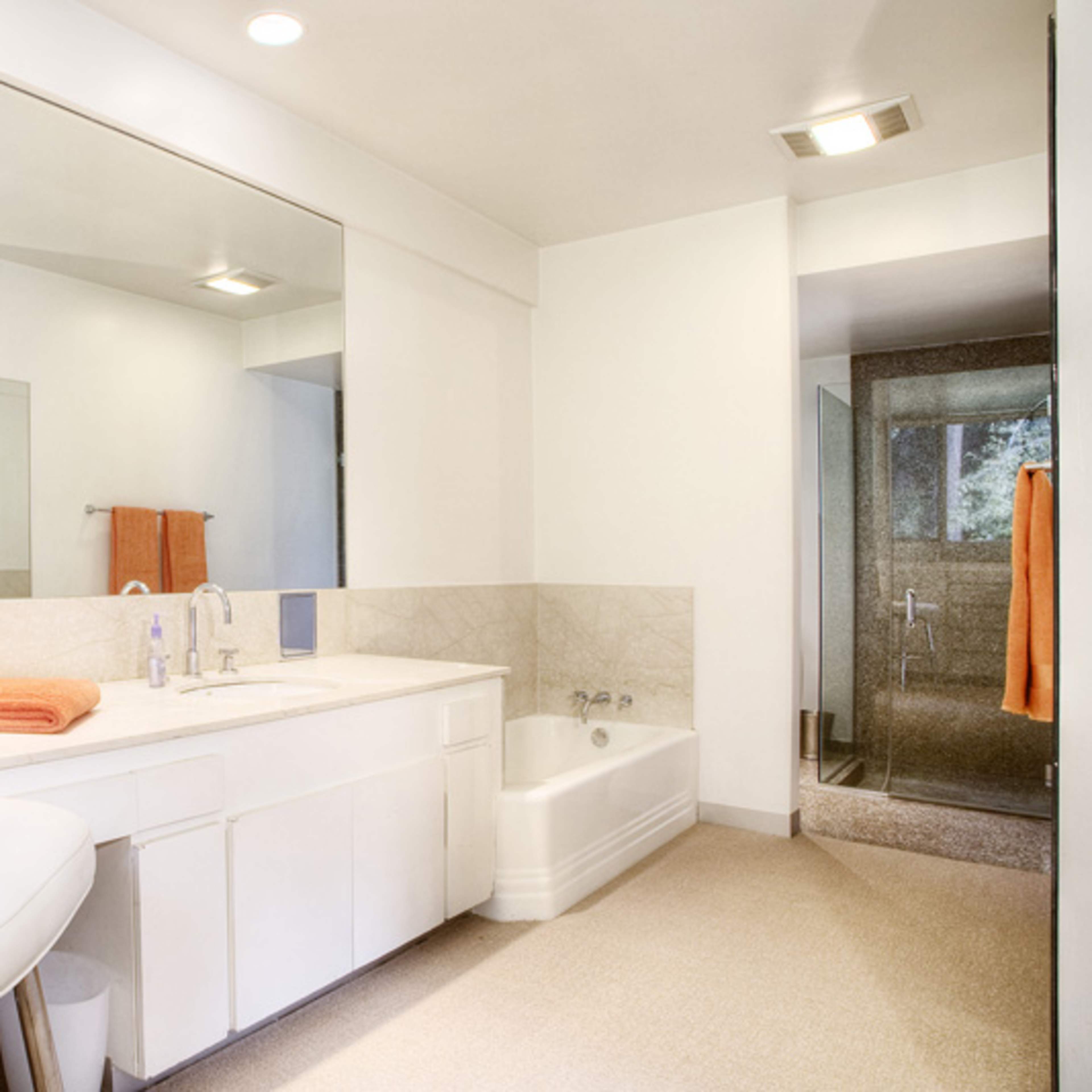 A modern bathroom with a double vanity, a large mirror, a walk-in shower, and a chair beside the sink.
