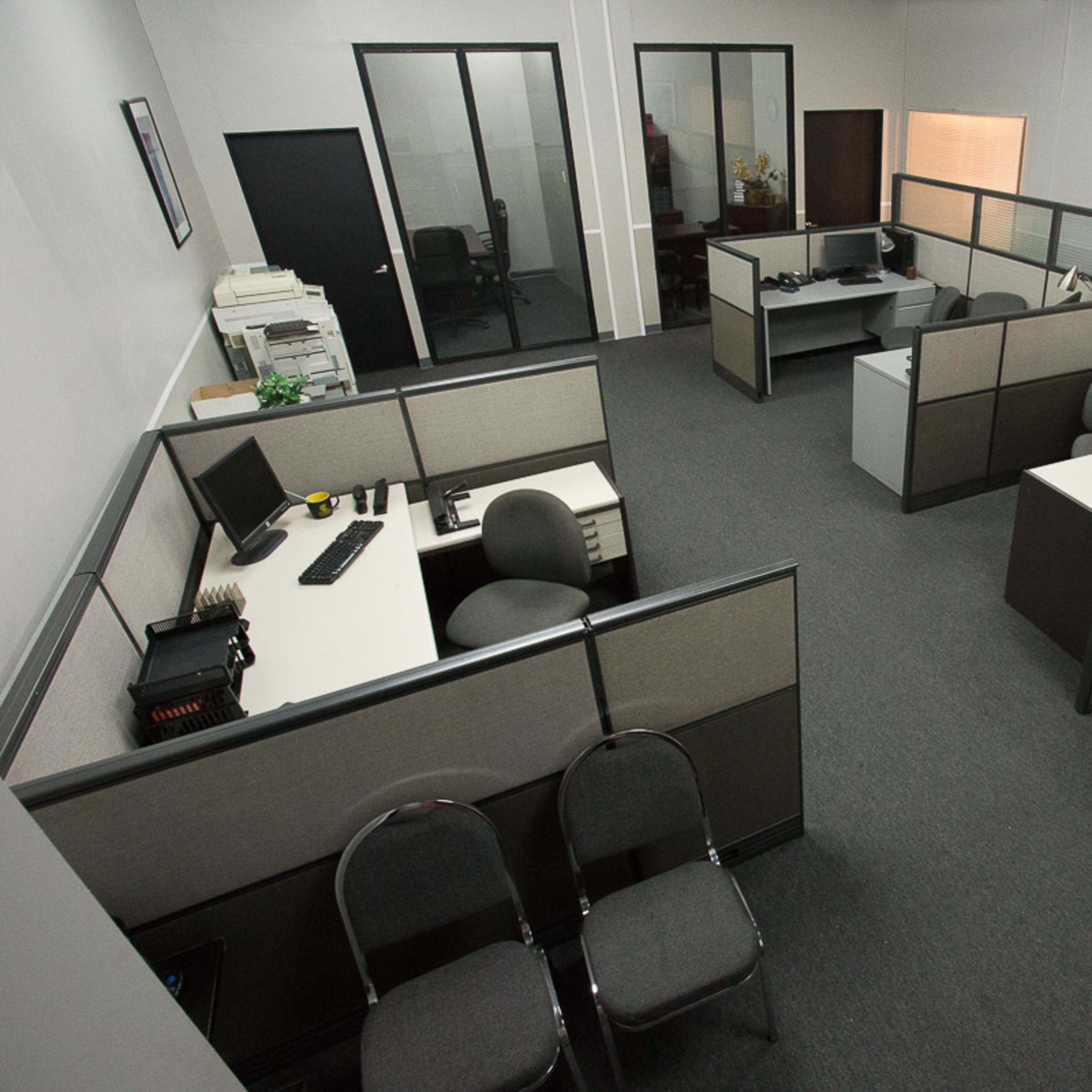 A spacious office layout with several workstations separated by cubicle partitions, featuring desks, chairs, and office equipment.