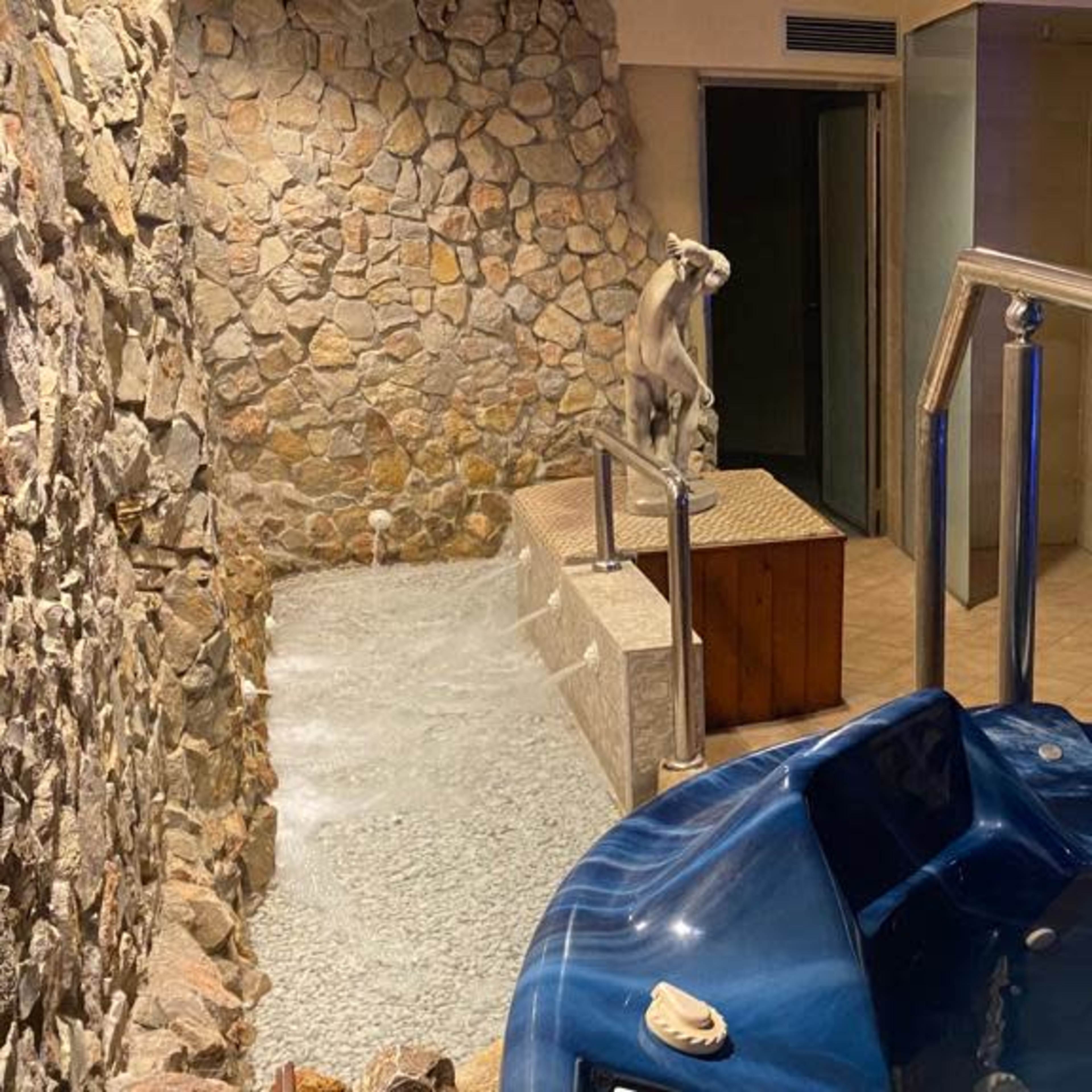 A spa area featuring a stone wall, a large blue hot tub, and a small stone water channel with a statue nearby.