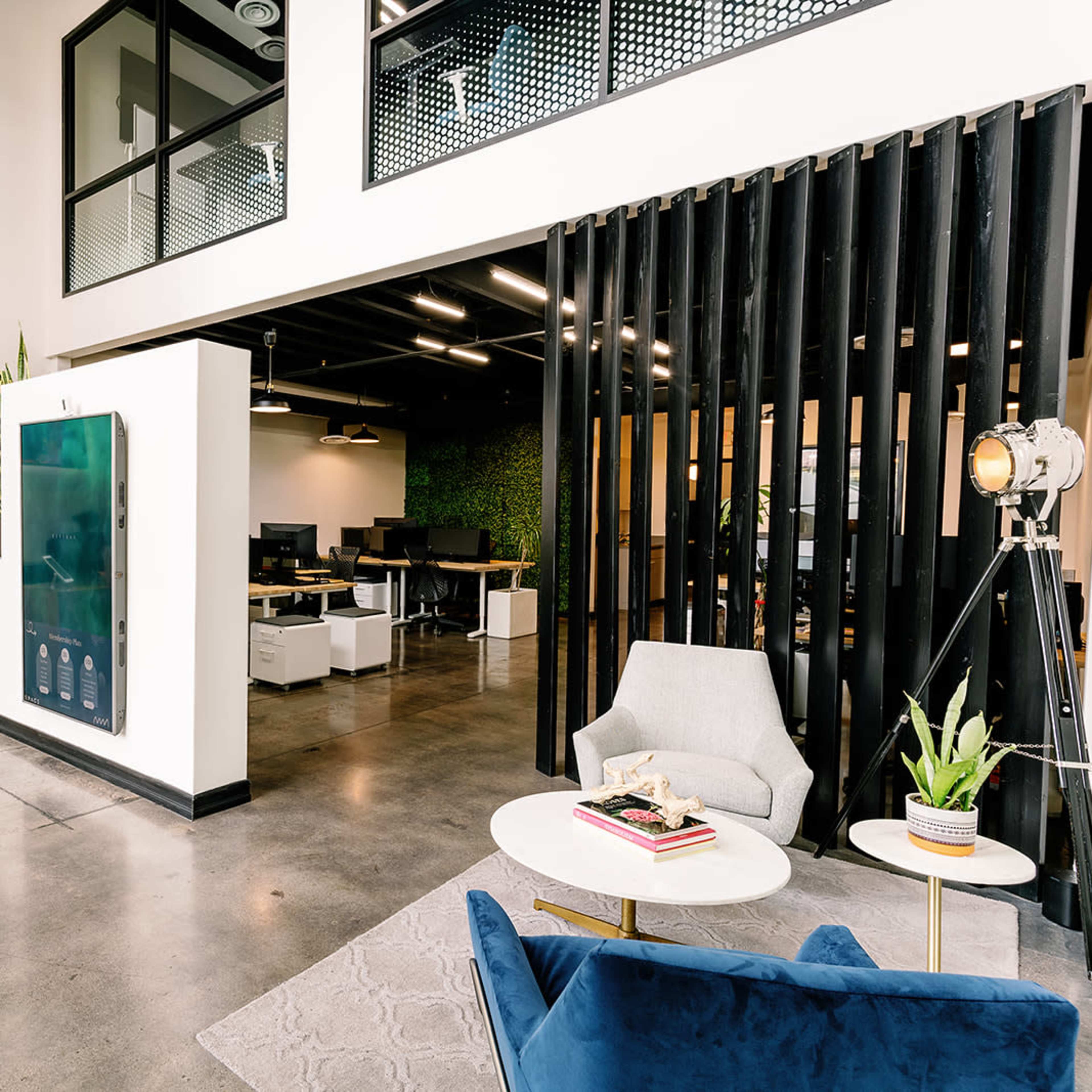 A modern office reception area featuring a large digital display, a wooden reception desk, and stylish seating arrangements with plants.