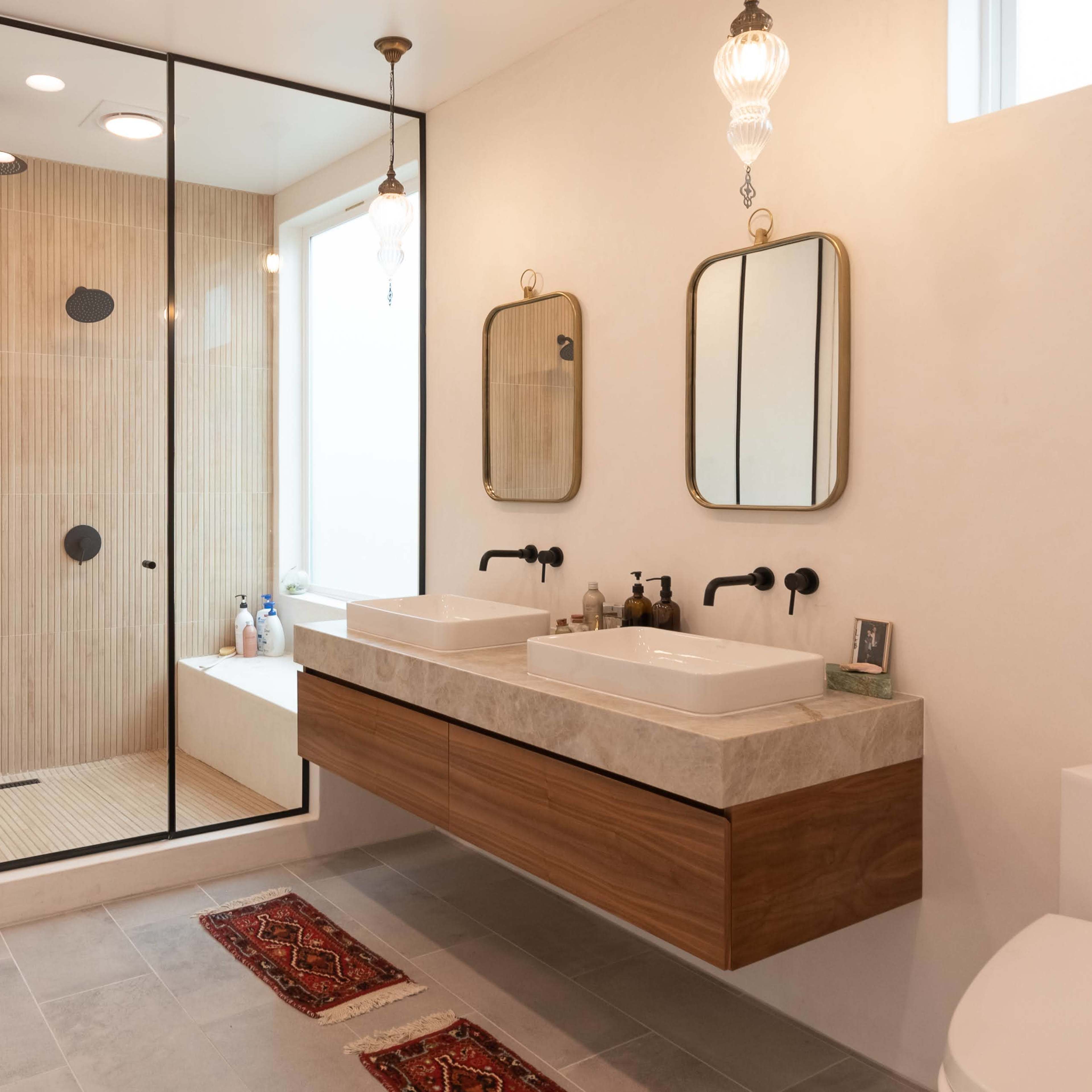 A modern bathroom featuring a glass-enclosed shower area, double sinks with a wooden vanity, and two mirrors above the sinks.