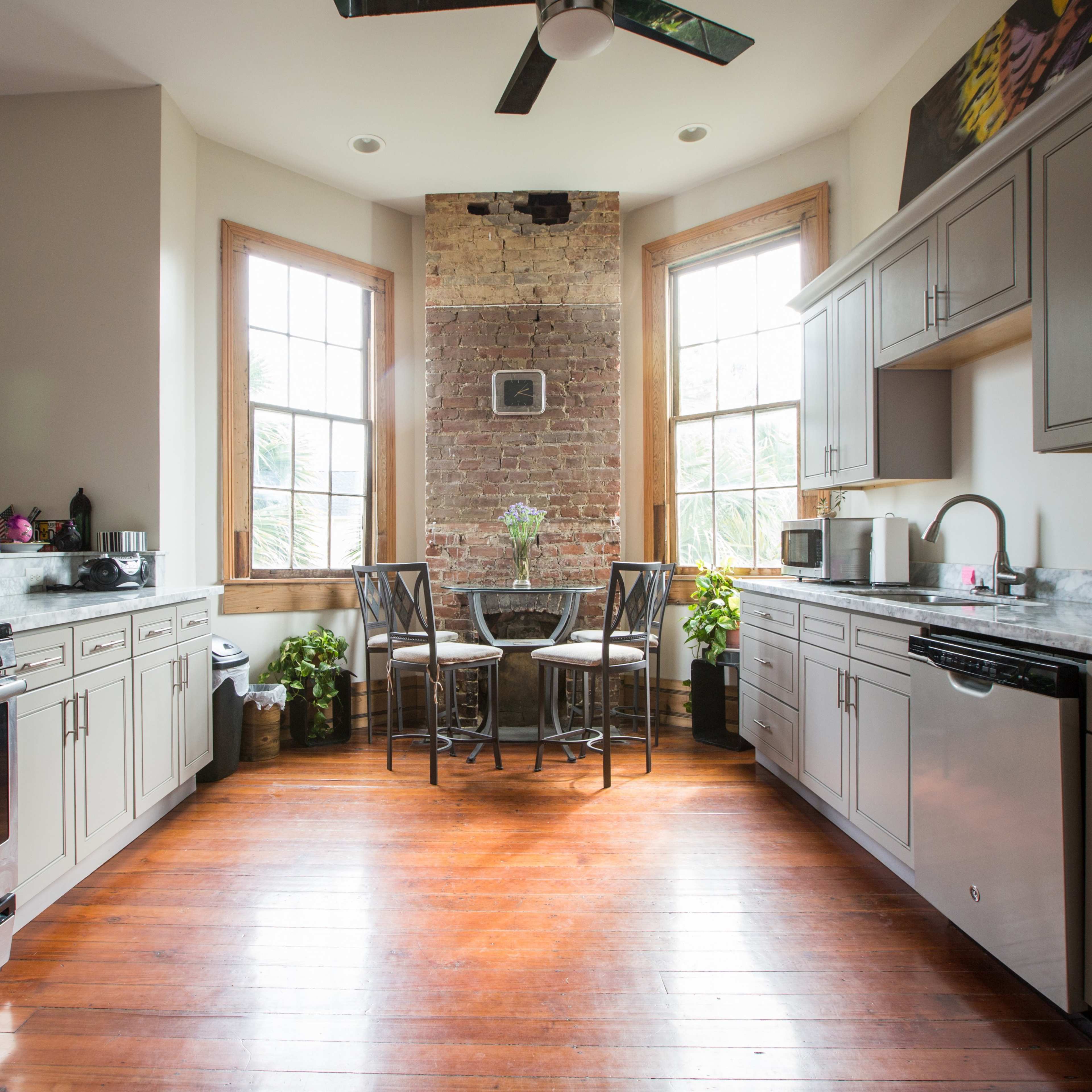 The kitchen features a combination of modern appliances and a rustic brick wall, with a small dining table set near large windows.