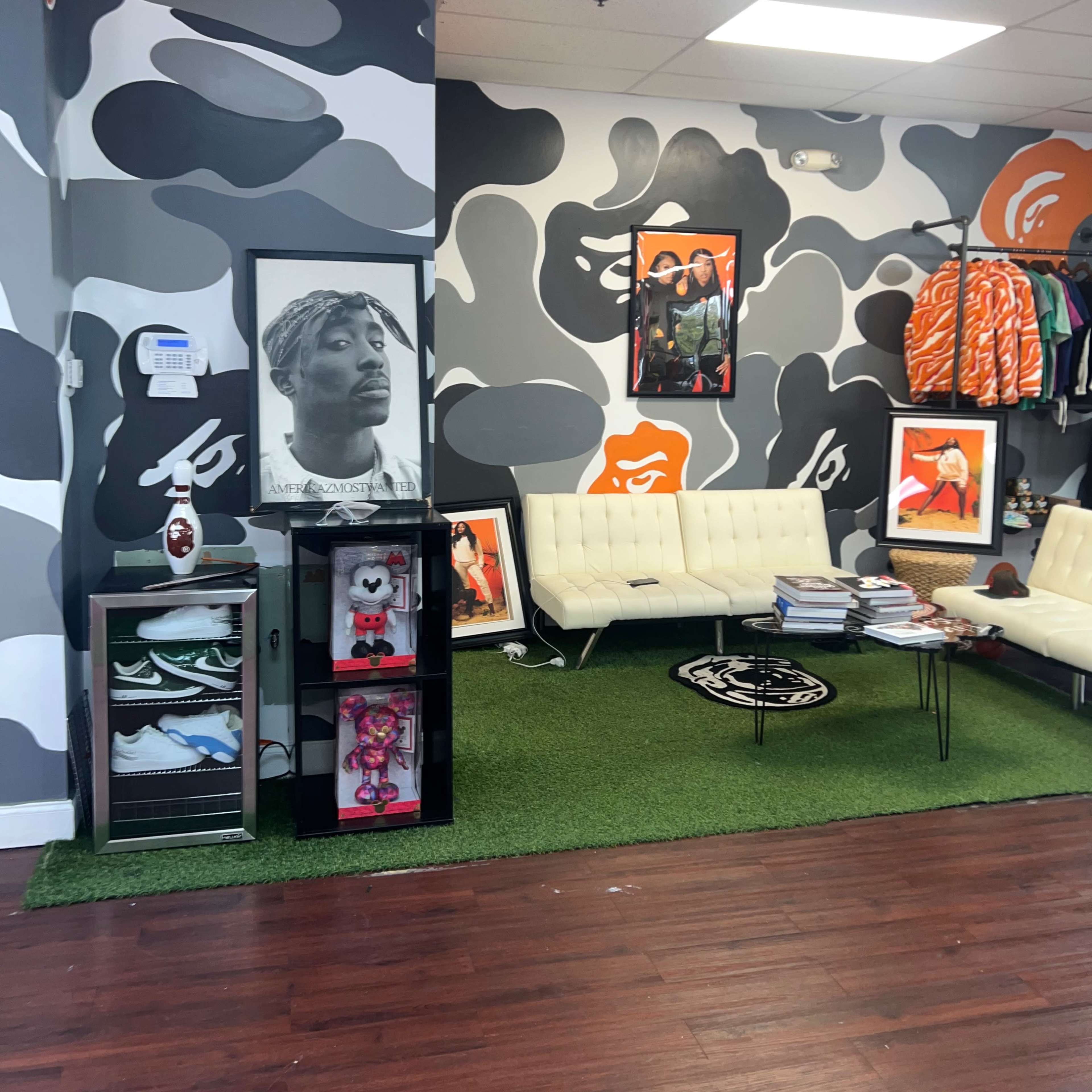 The interior of a retail store features a camouflaged wall design, with framed pictures on the walls and a green carpet area with seating and display cases.