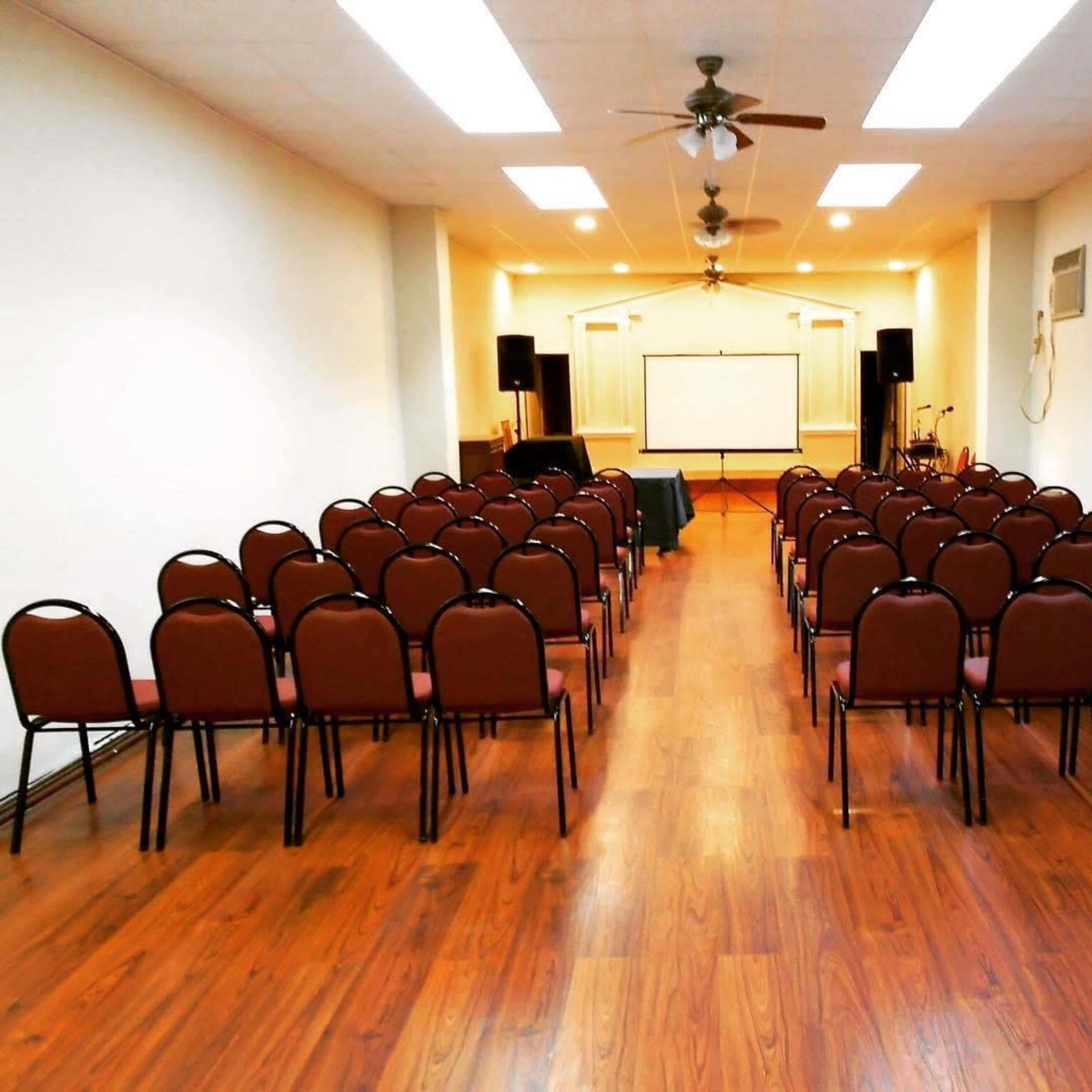 An empty event space arranged with rows of brown chairs facing a blank screen at the front of the room.