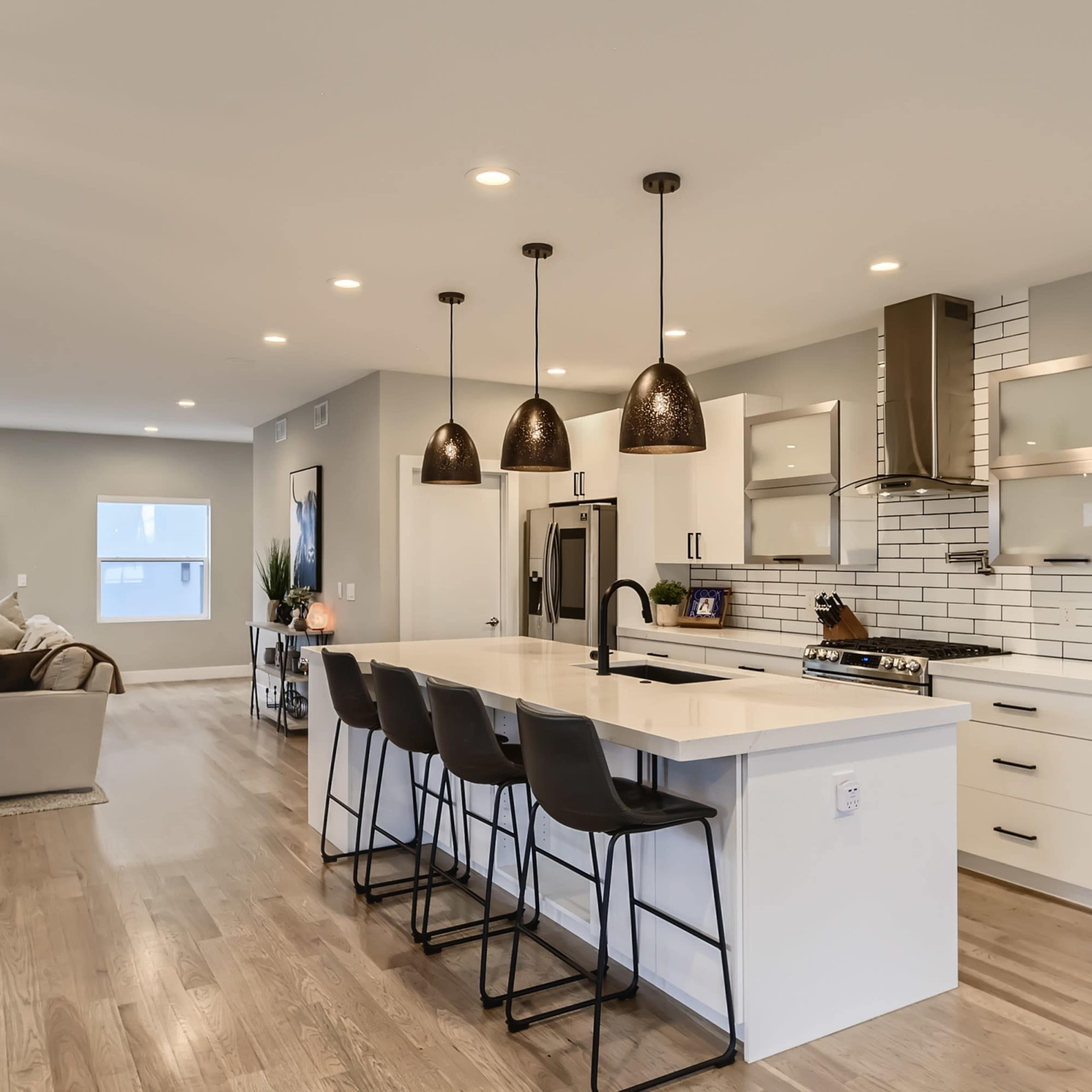A modern kitchen featuring white cabinetry, a subway tile backsplash, a large island with bar stools, and pendant lighting.