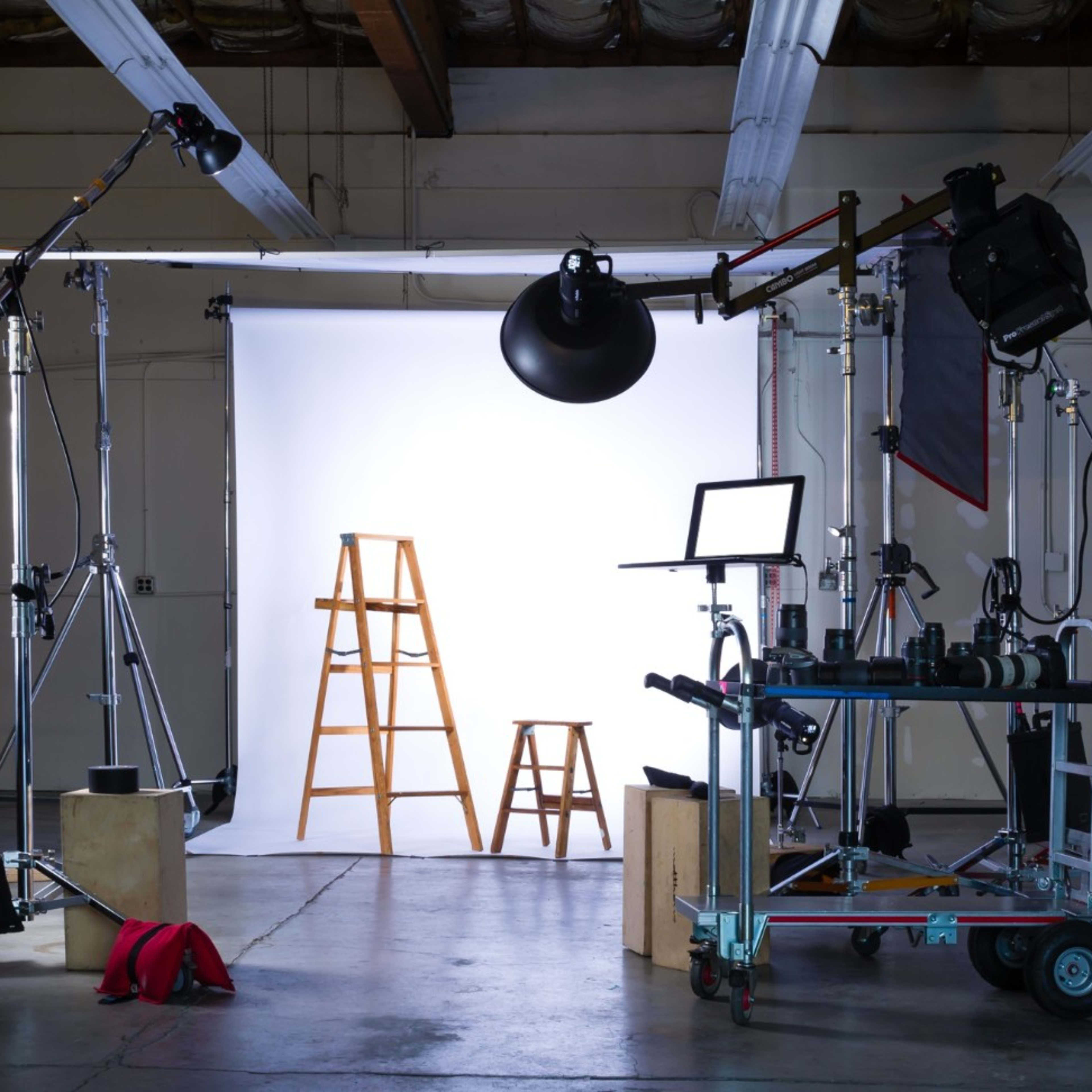 A photography studio setup with two ladders, multiple light sources, and various equipment arranged around a backdrop.